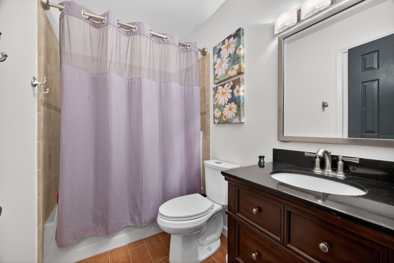 Bathroom with purple shower curtain, white toilet, dark wood vanity with sink, large mirror, and hardwood floors.