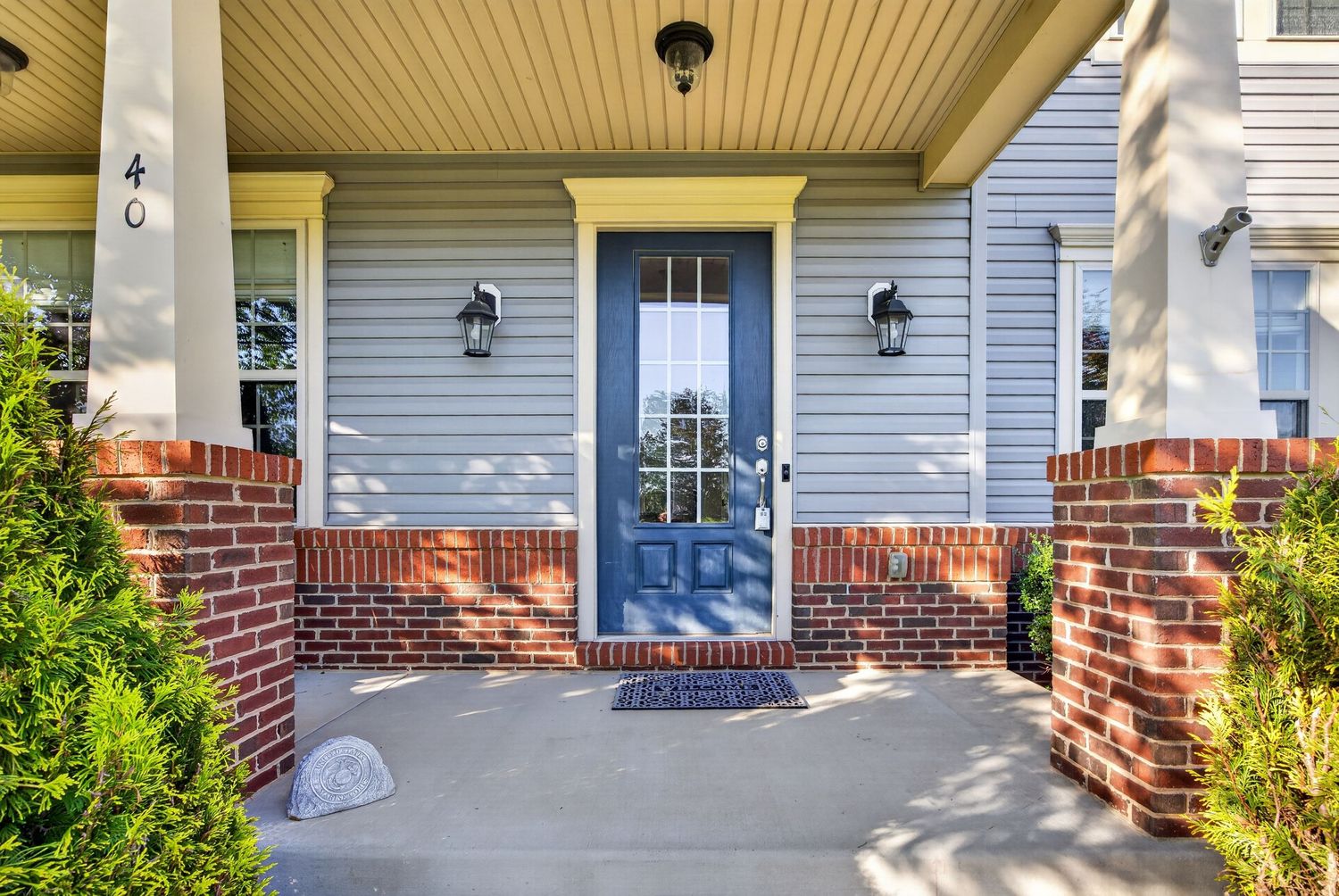 Charming home entryway with blue front door, brick pillars, wall lanterns, and a covered porch at number 40.