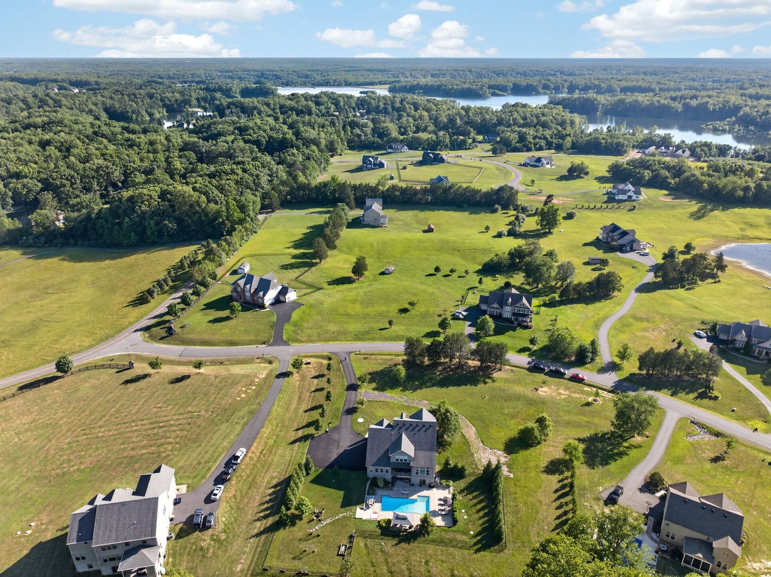 Aerial view of a luxury residential community with spacious green lots, scattered homes, a pool, and a scenic lake backdrop.