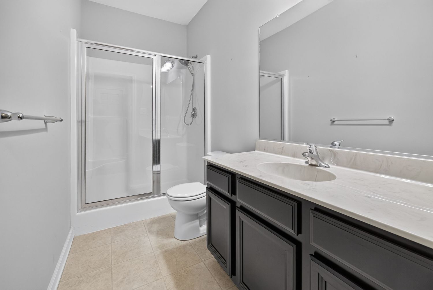 Modern bathroom with dark vanity, white countertop, walk-in shower, toilet, and large mirror on light gray walls.