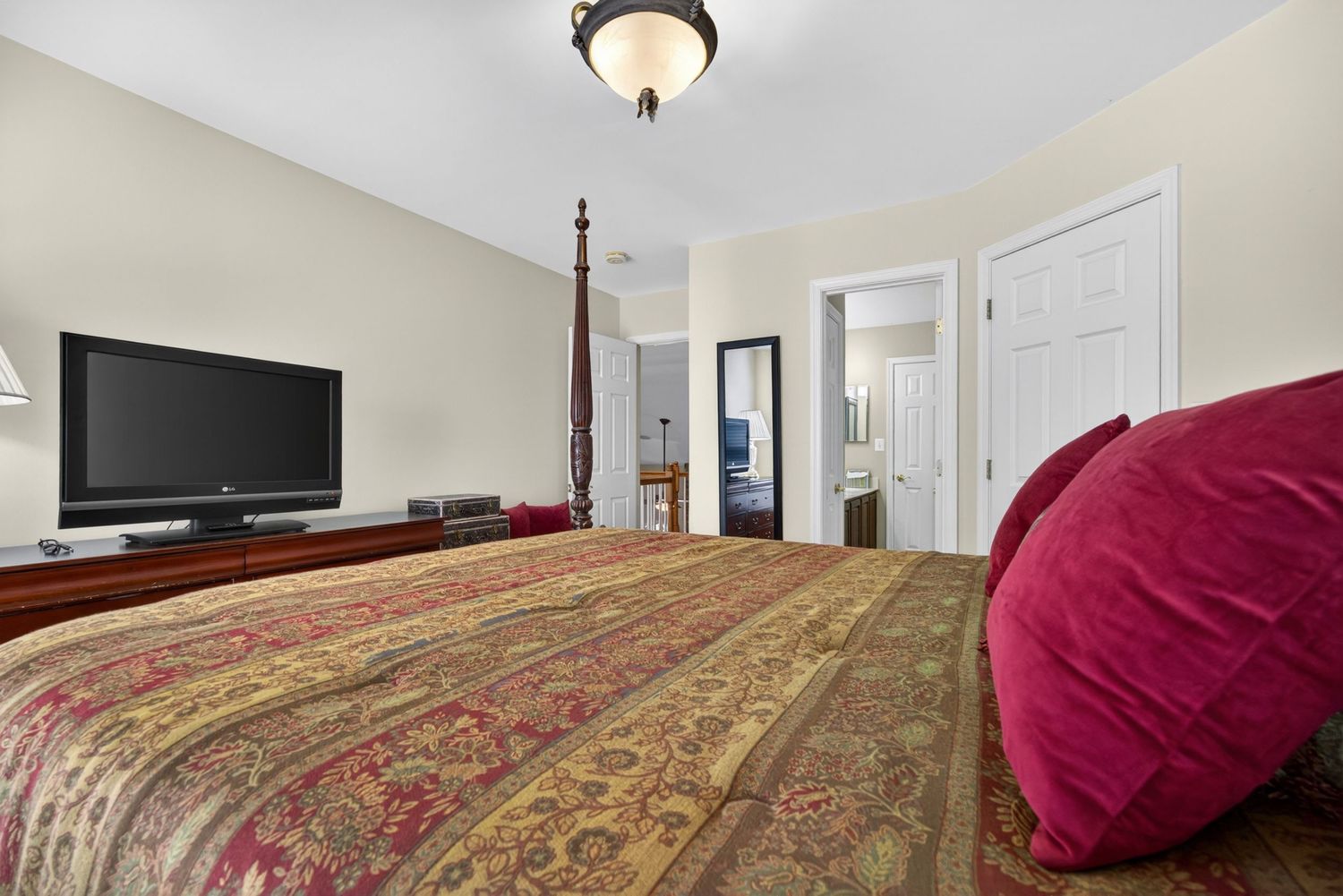Elegant bedroom with a four-poster bed, patterned bedspread, flat-screen TV, and an open doorway leading to an ensuite.