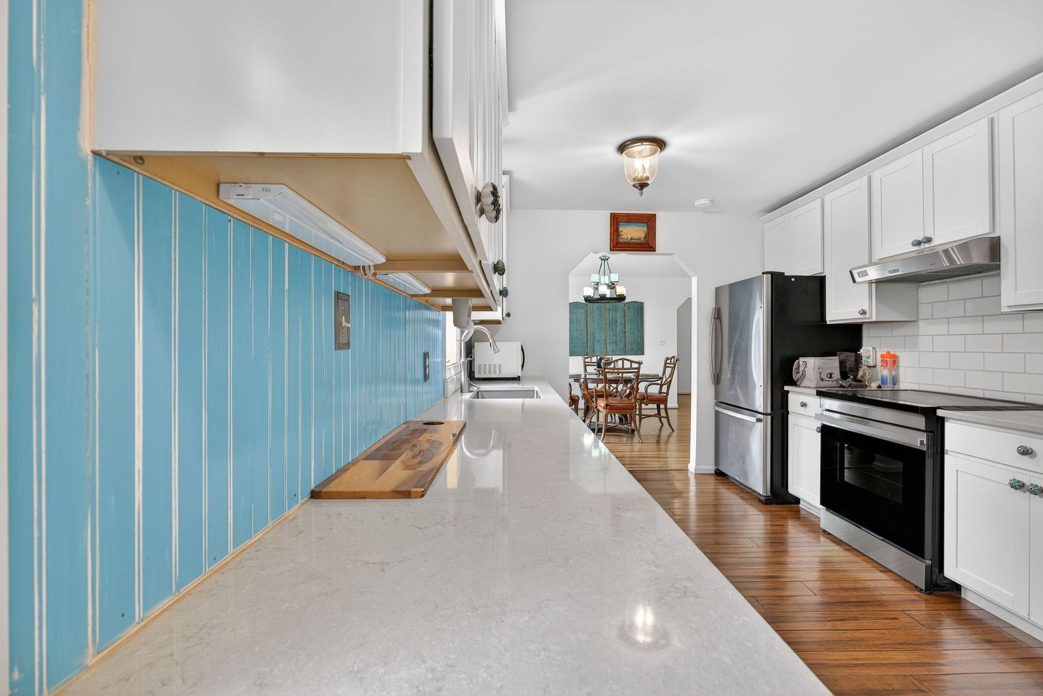 Bright kitchen with white cabinets, granite countertops, stainless steel appliances, and blue accent wall leading to dining area.