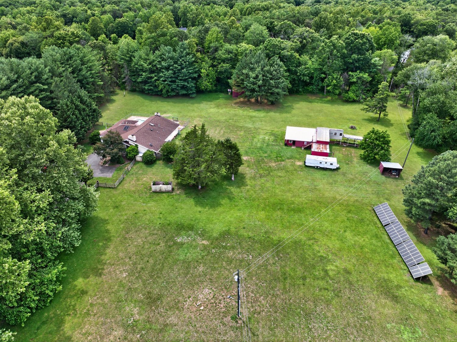 Aerial view of a rural property with a house, red barn, solar panels, and lush green trees surrounding open lawn.