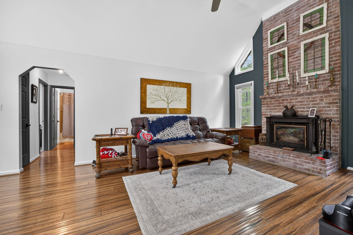Cozy living room with hardwood floors, brick fireplace, vaulted ceilings, and leather sofa with coffee table.