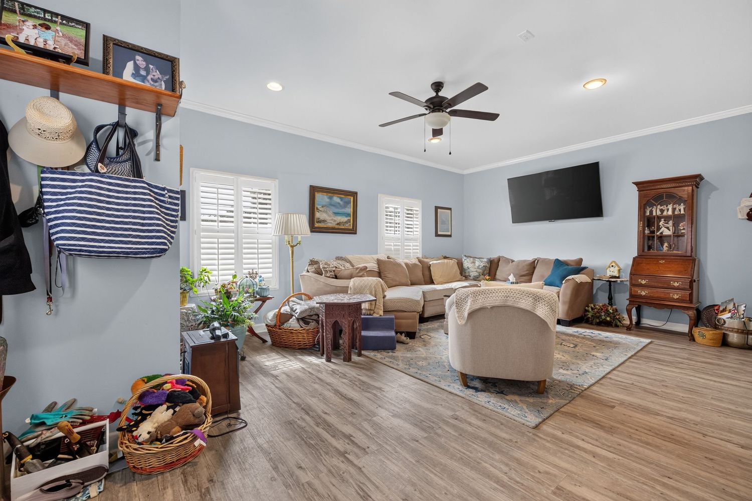 Bright living room with light blue walls, hardwood floors, beige sectional sofa, ceiling fan, and wall-mounted TV.