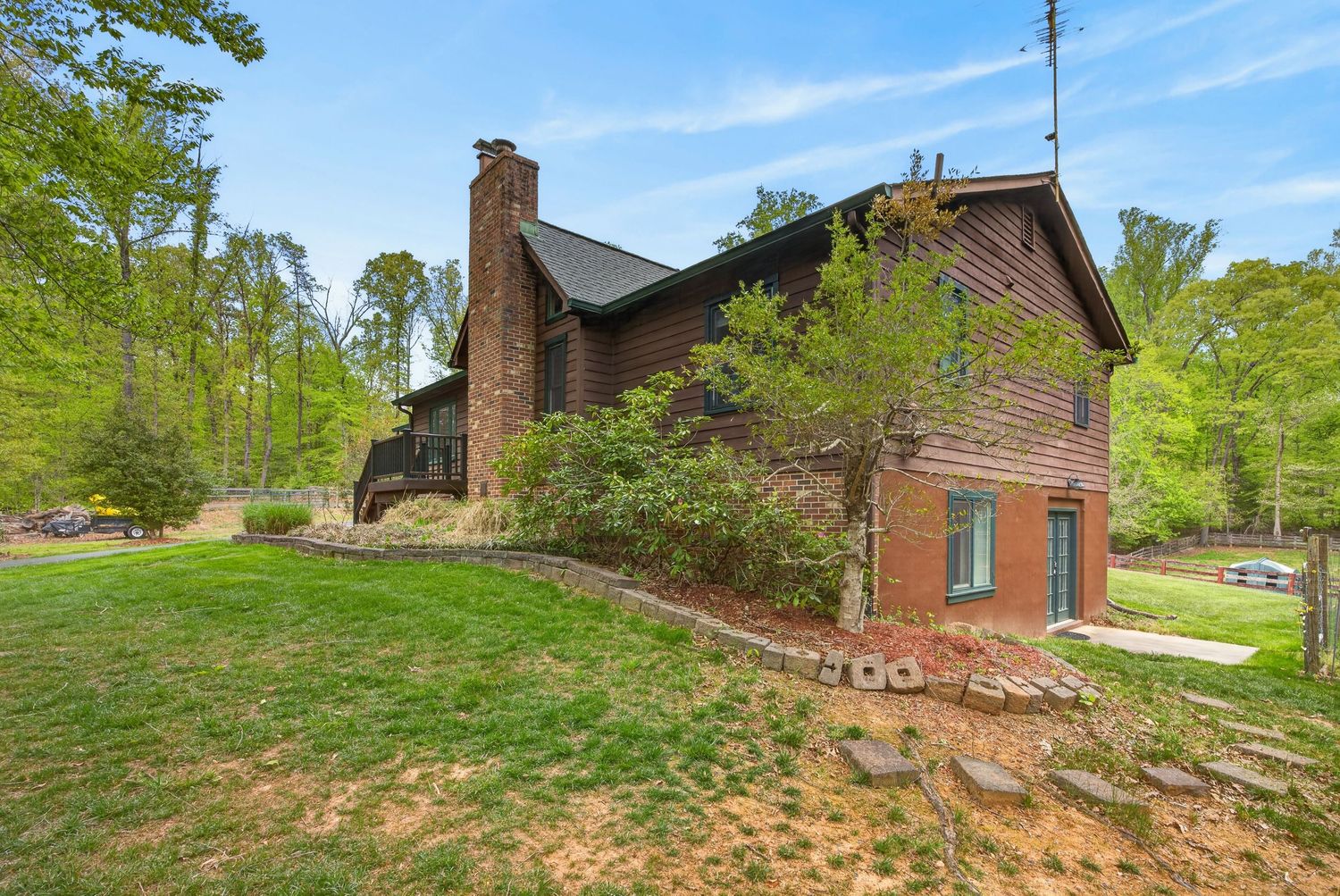 Rustic brick house with chimney surrounded by lush green trees and landscaped yard in spring.