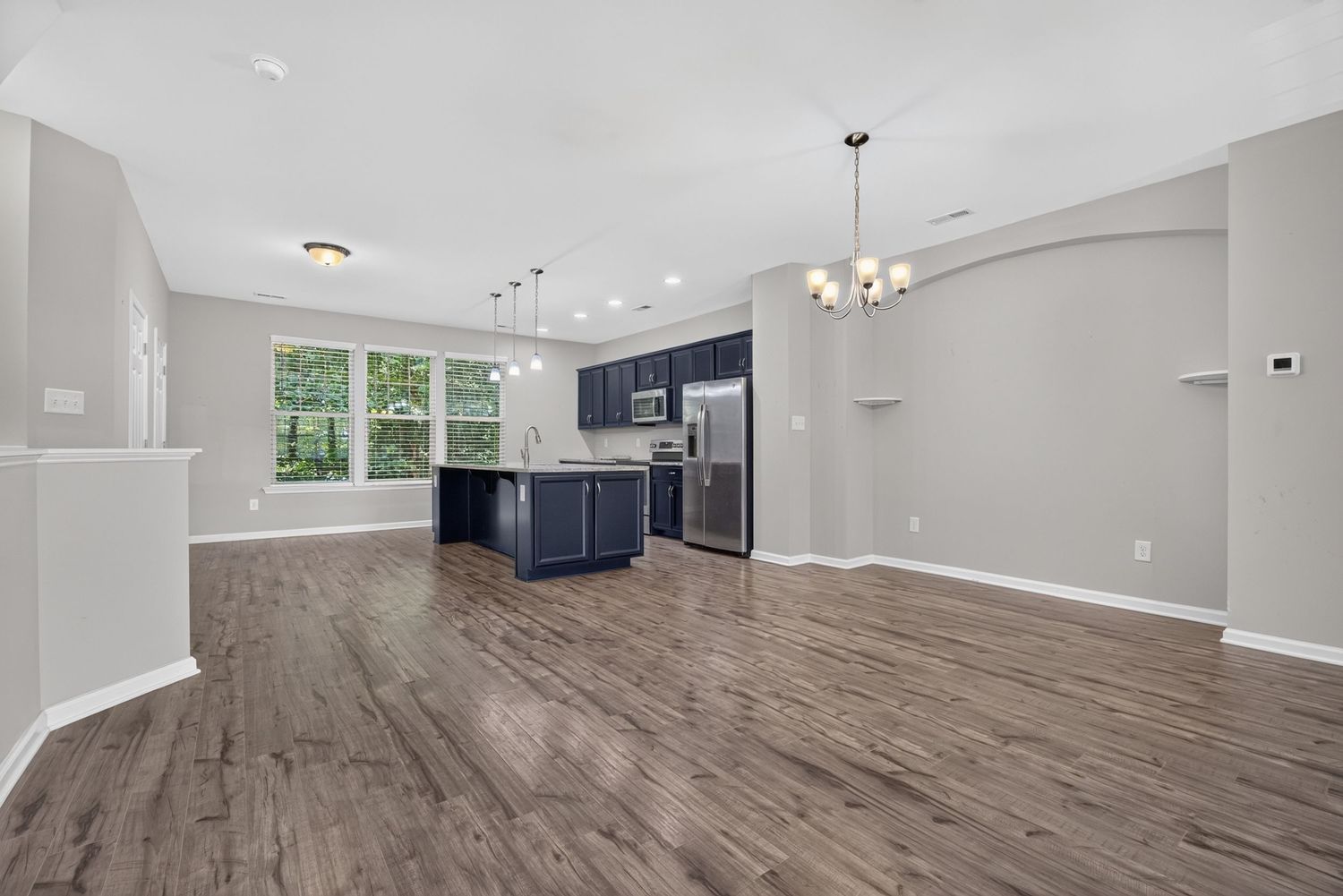 Open-concept living area with dark hardwood floors, navy blue kitchen cabinets, stainless steel appliances, and modern chandelier lighting.