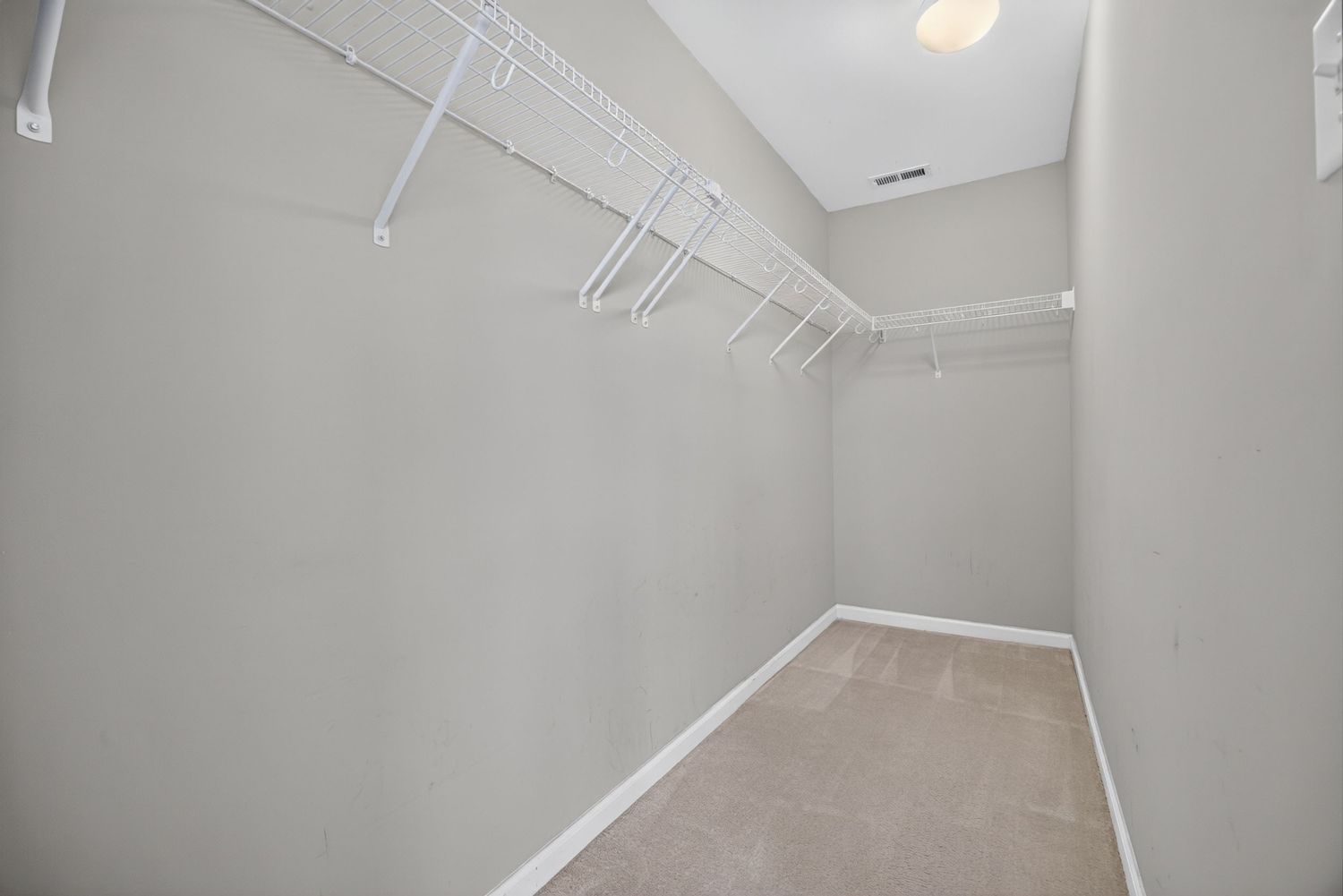 Spacious walk-in closet with white wire shelving, neutral carpet, and gray walls in a modern home.