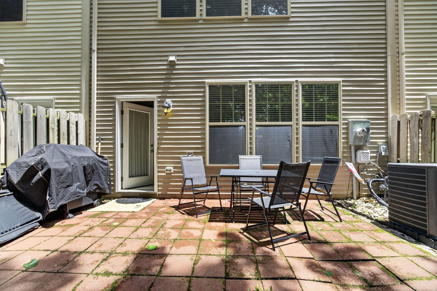 Patio with brick pavers, outdoor dining set, covered grill, and AC unit beside a beige siding home.