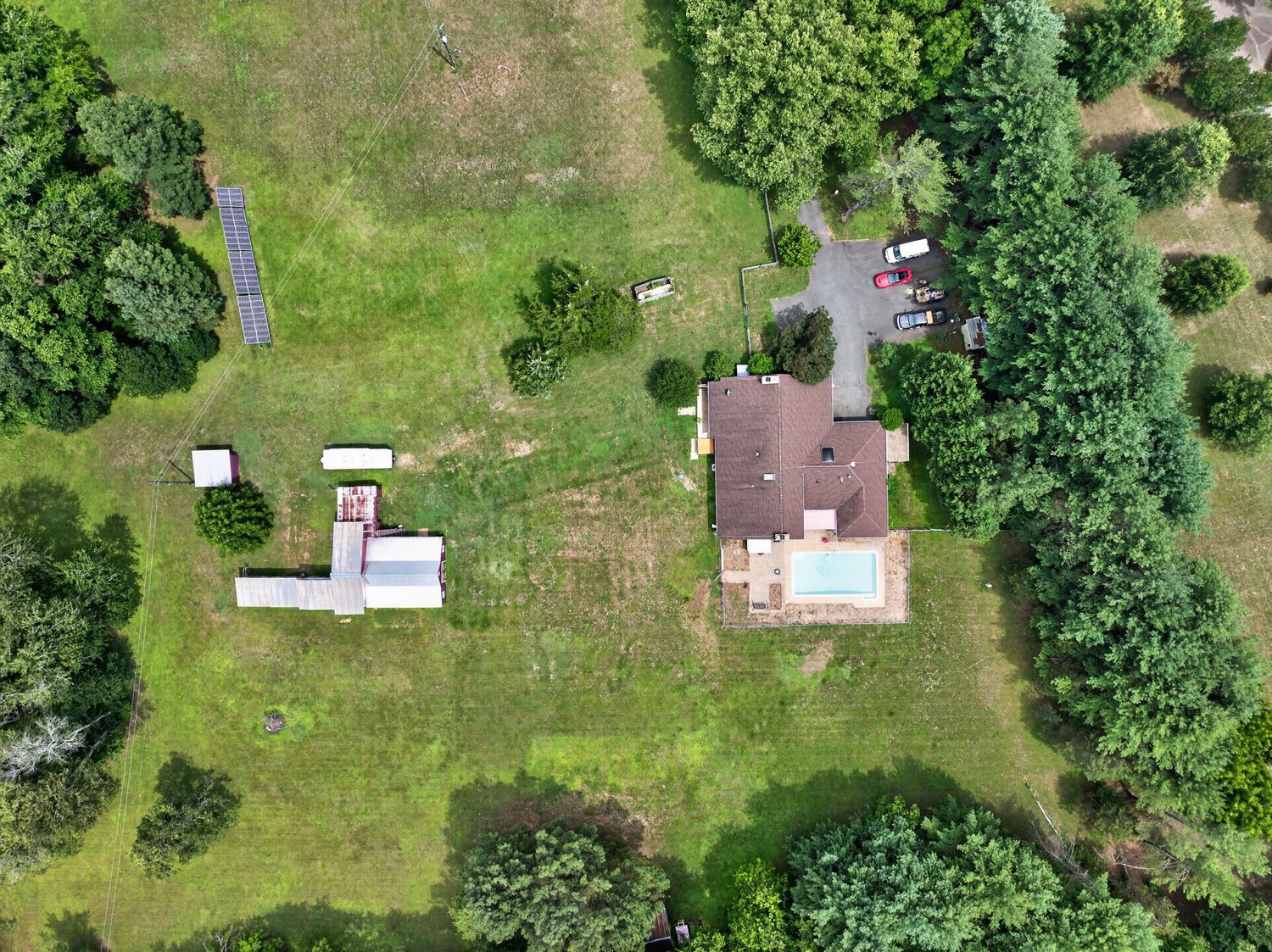 Aerial drone view of a rural property featuring a house with pool, outbuildings, and lush green surrounding landscape.