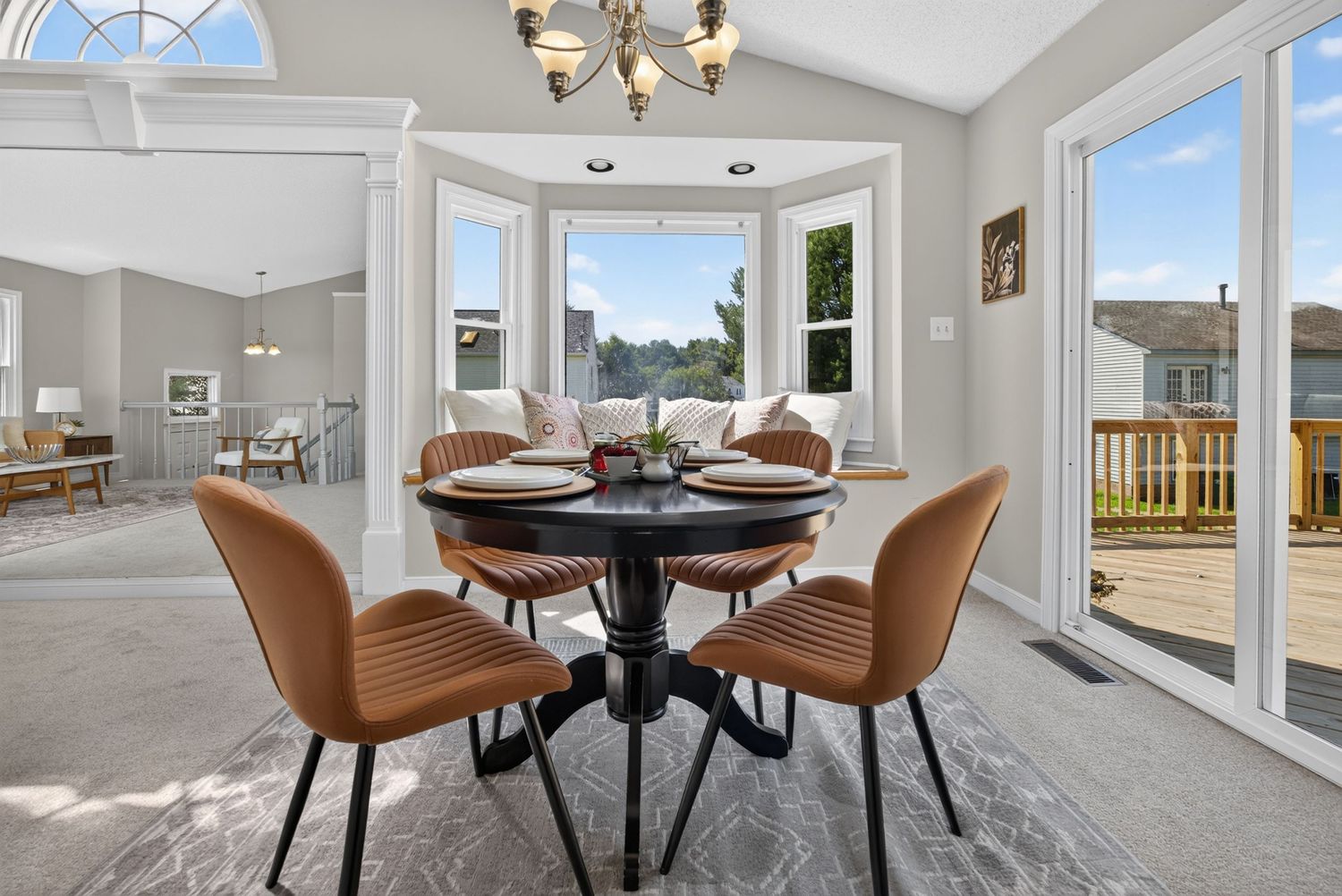 Bright dining area with round black table, tan leather chairs, bay window, and sliding glass door to deck.