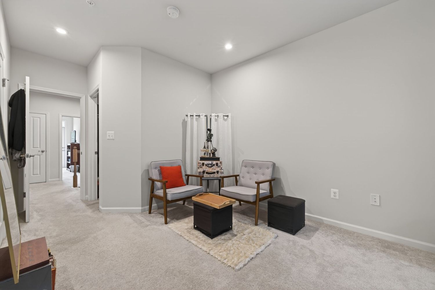 Bright living room with gray carpet, two mid-century chairs, small coffee table, and recessed lighting in a modern home.