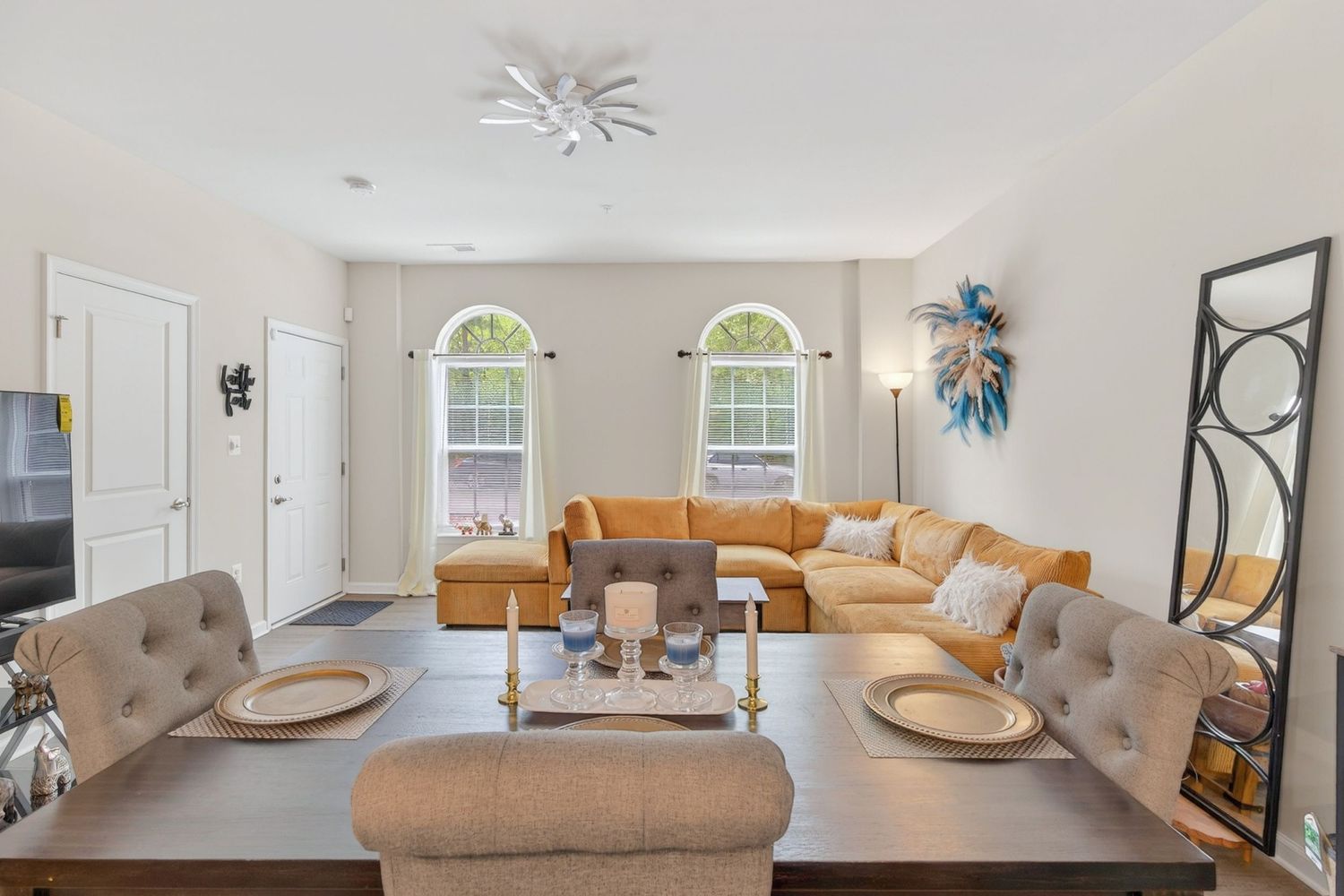 Bright living room with orange sectional sofa, arched windows, ceiling fan, and dining table in an open floor plan.