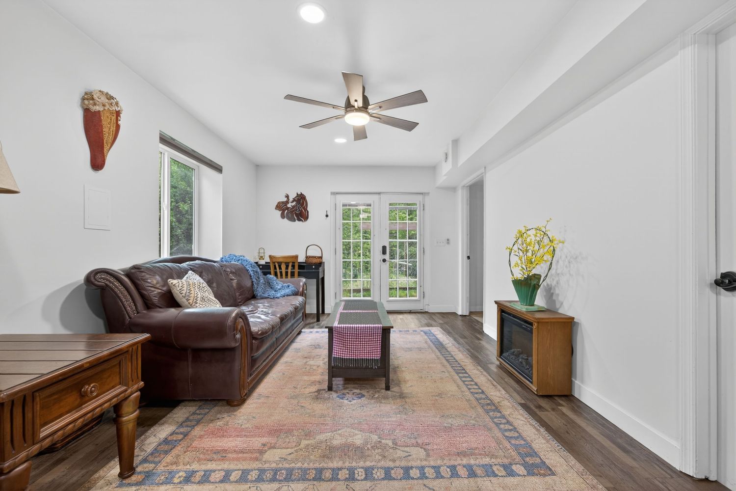 Cozy living room with leather sofa, ceiling fan, hardwood floors, Persian rug, and French doors letting in natural light.