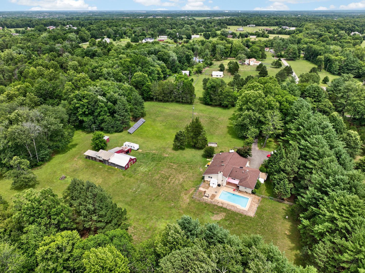 Aerial view of a spacious suburban property with a pool, open lawn, and surrounded by lush green trees.