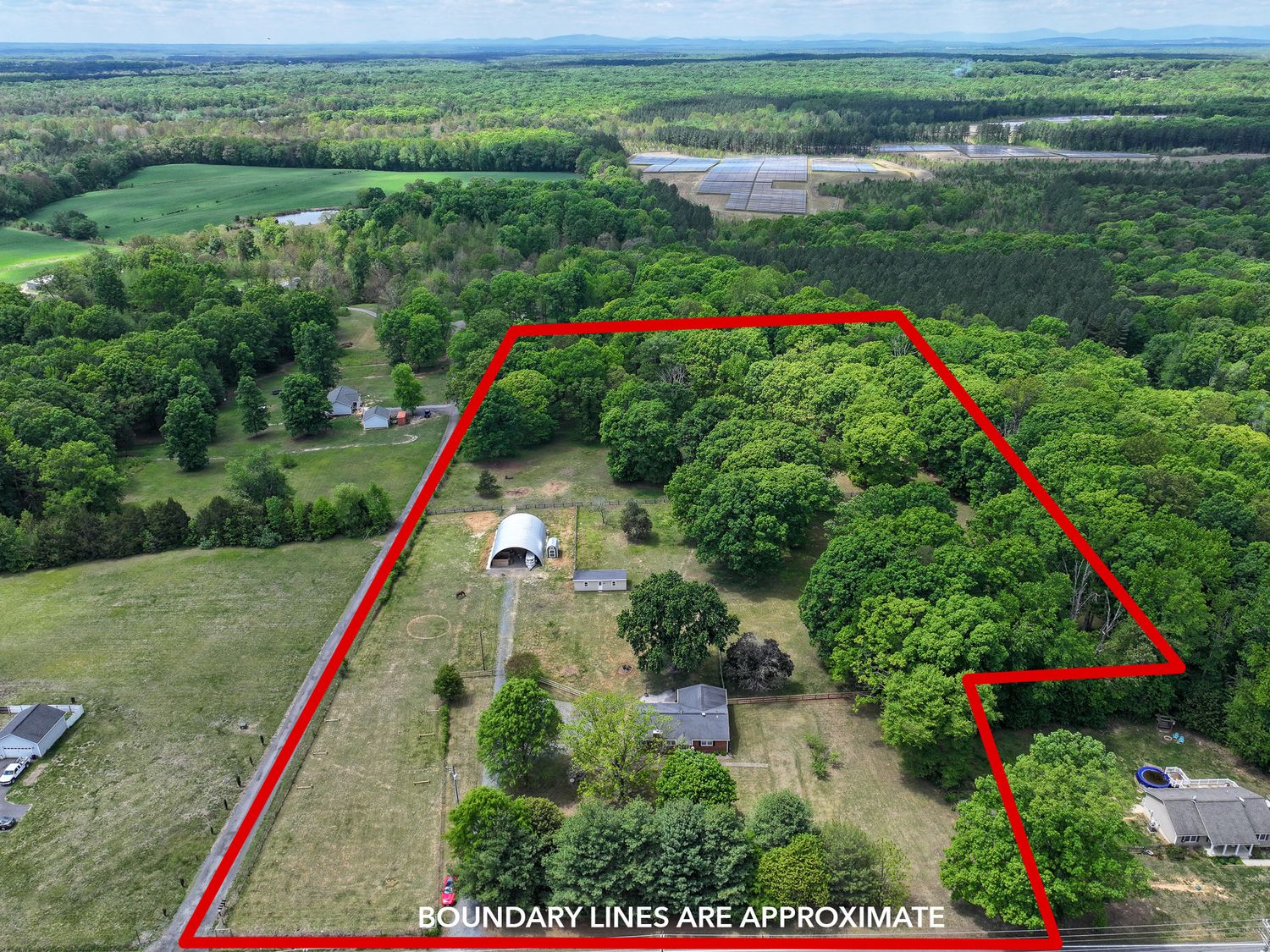 Aerial view of a rural property with approximate boundary lines marked in red, featuring a barn, trees, and open land.