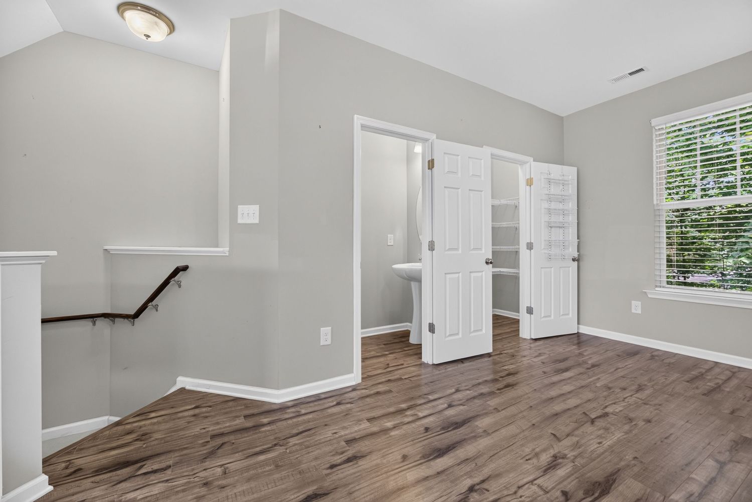 Spacious bedroom with dark hardwood floors, white bi-fold closet doors, and a bright window in a modern home.