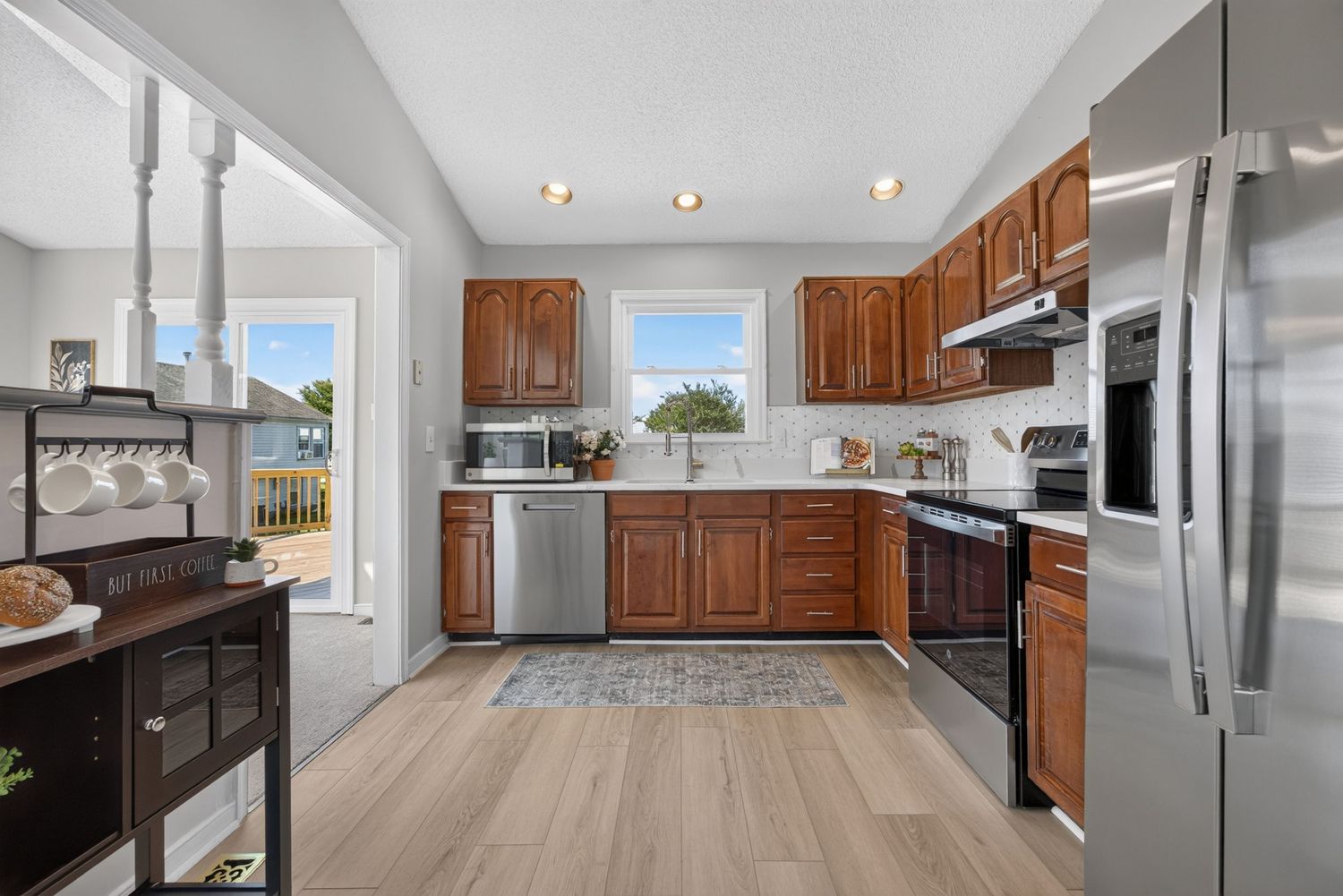 Bright kitchen with brown cabinets, stainless steel appliances, light hardwood floors, and a window above the sink.