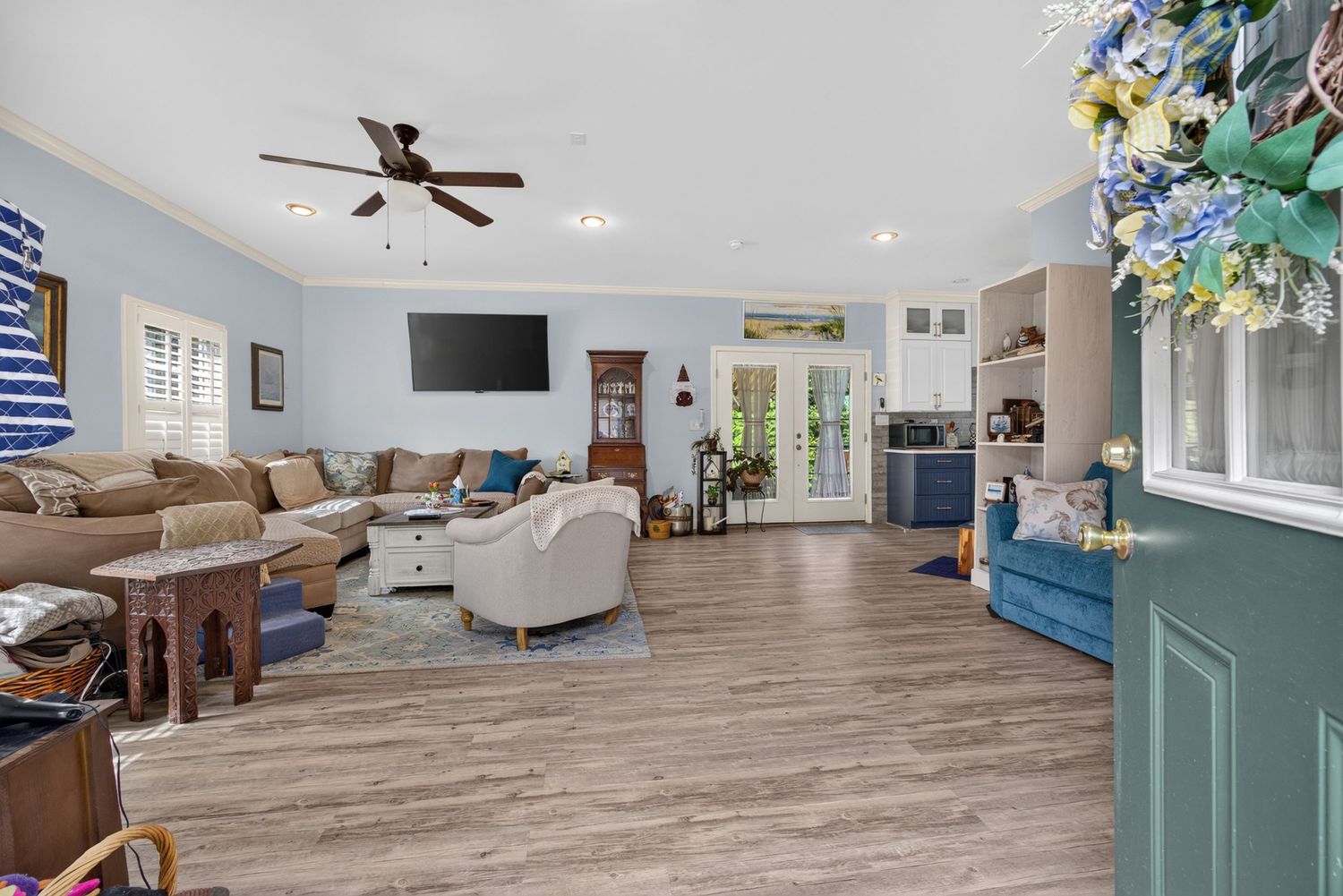 Spacious living room with light wood floors, blue walls, ceiling fan, wall-mounted TV, and French doors leading outside.