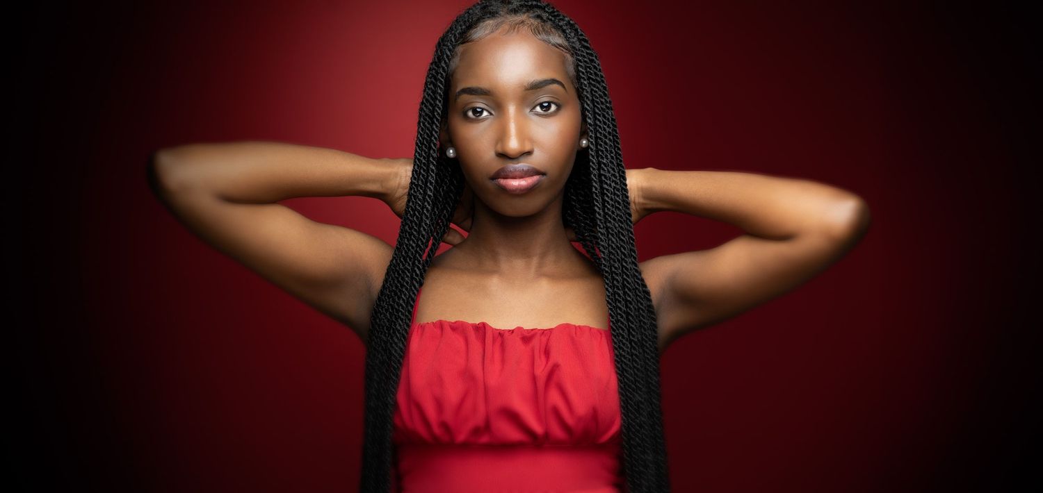 Dramatic portrait of person in red top with long braids against burgundy background.