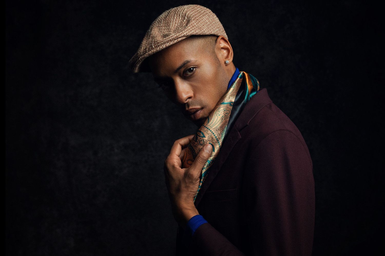 Artistic portraits featuring a cap and burgundy jacket in moody studio lighting.
