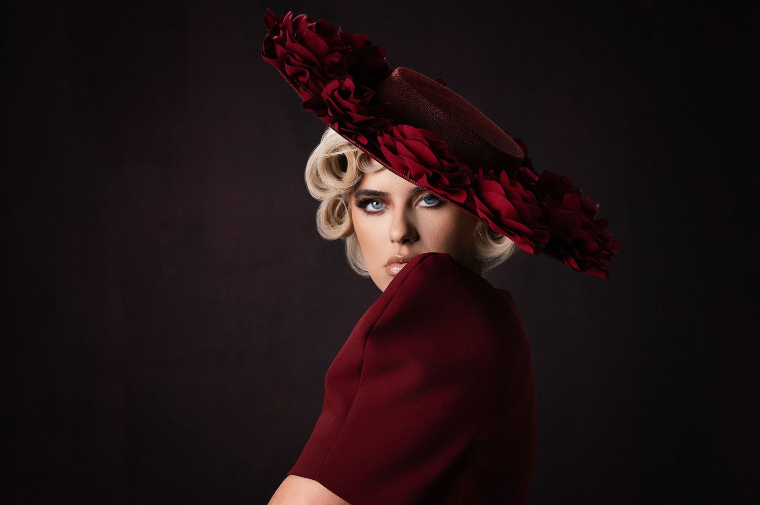 Dramatic portrait wearing burgundy hat and dress in moody lighting.