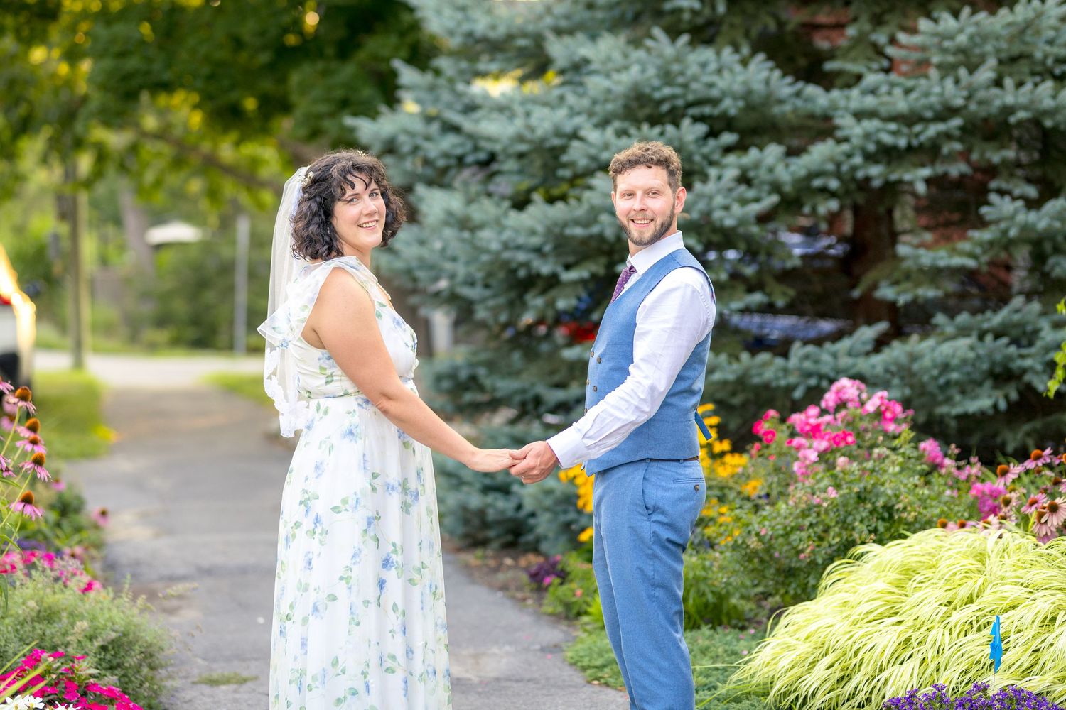 A eloping couple shares a romantic moment along a path setting surrounded by spruce trees and summer flowers. Ottawa Westboro Photographer