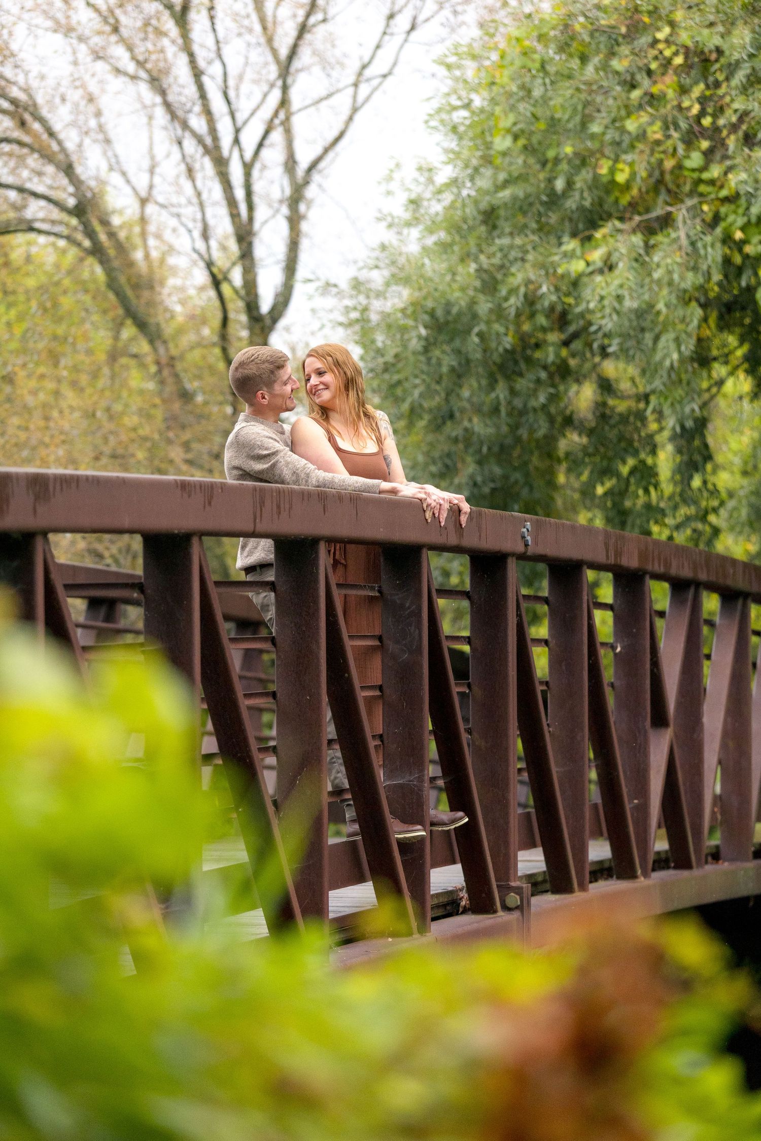 Couple posing on rustic wooden bridge with trees and foliage creating natural framing. Ottawa Wedding Photographer