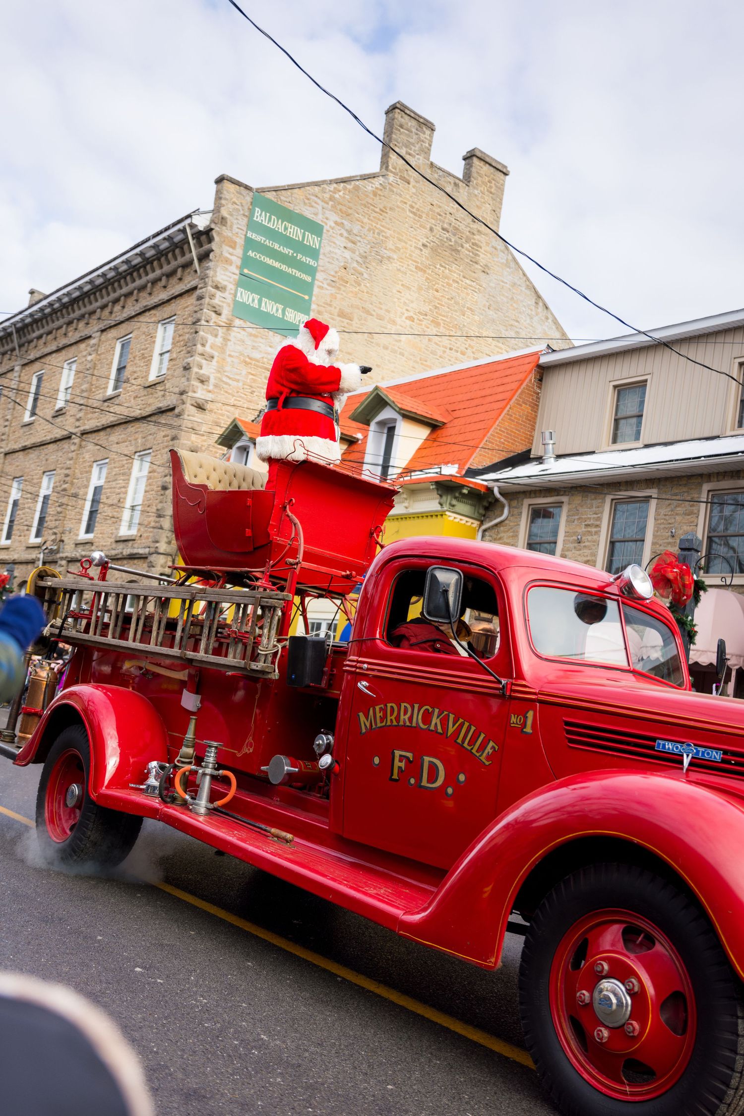 A vintage Middleville FD fire truck carries Santa Claus in his sleigh during a holiday parade on a small town street.