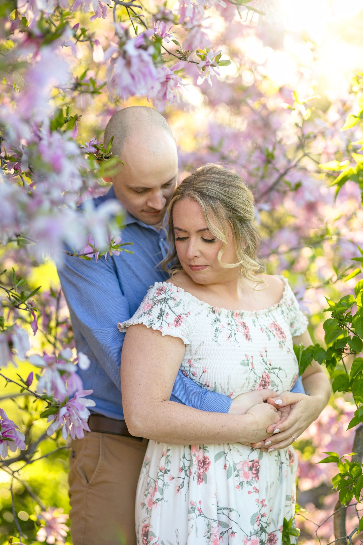 Tender embrace captured among pink spring blossoms during golden hour. Ottawa Wedding Photographer