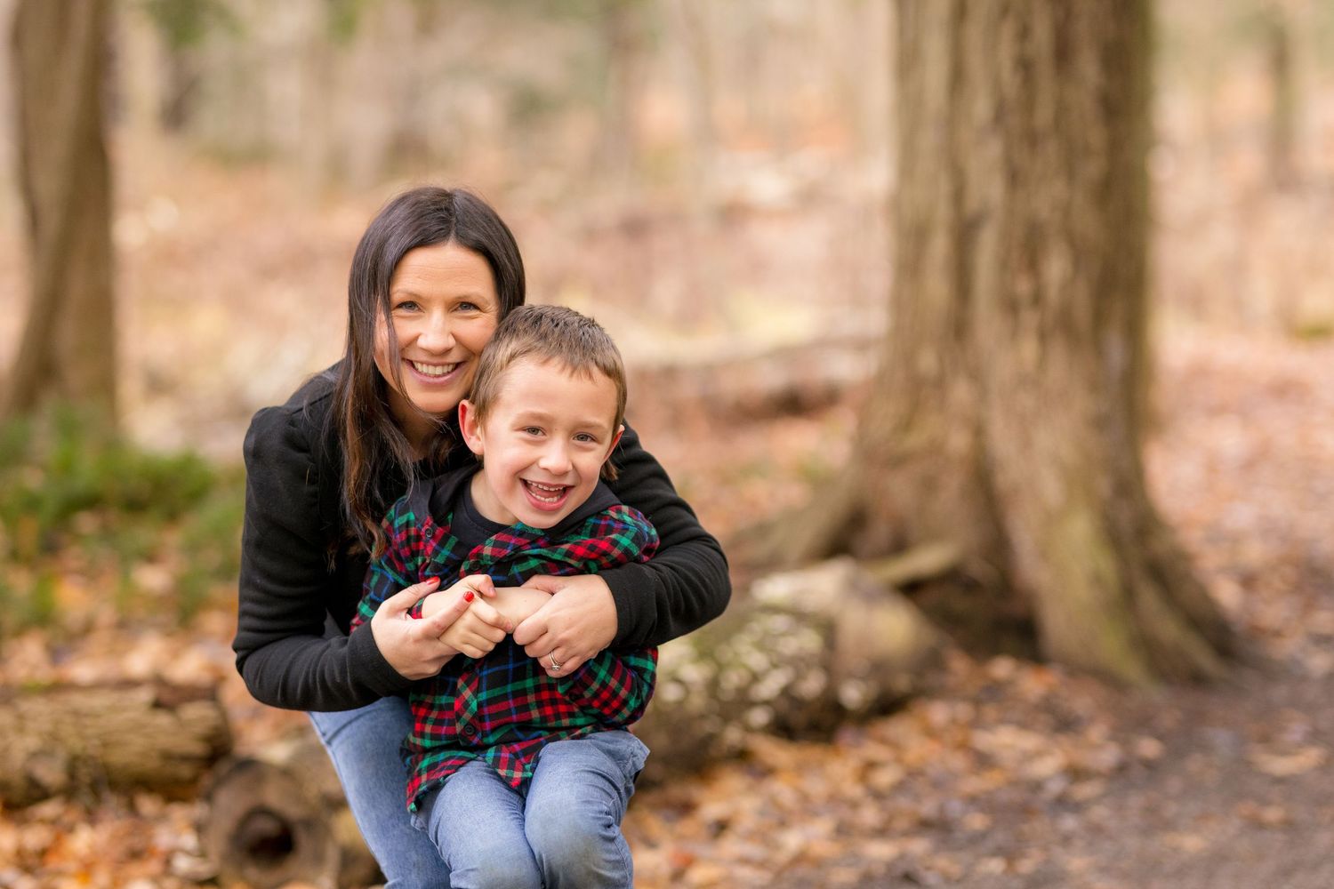 A family enjoys a casual autumn photo session among tall trees with fallen leaves. Ottawa Family Photographer