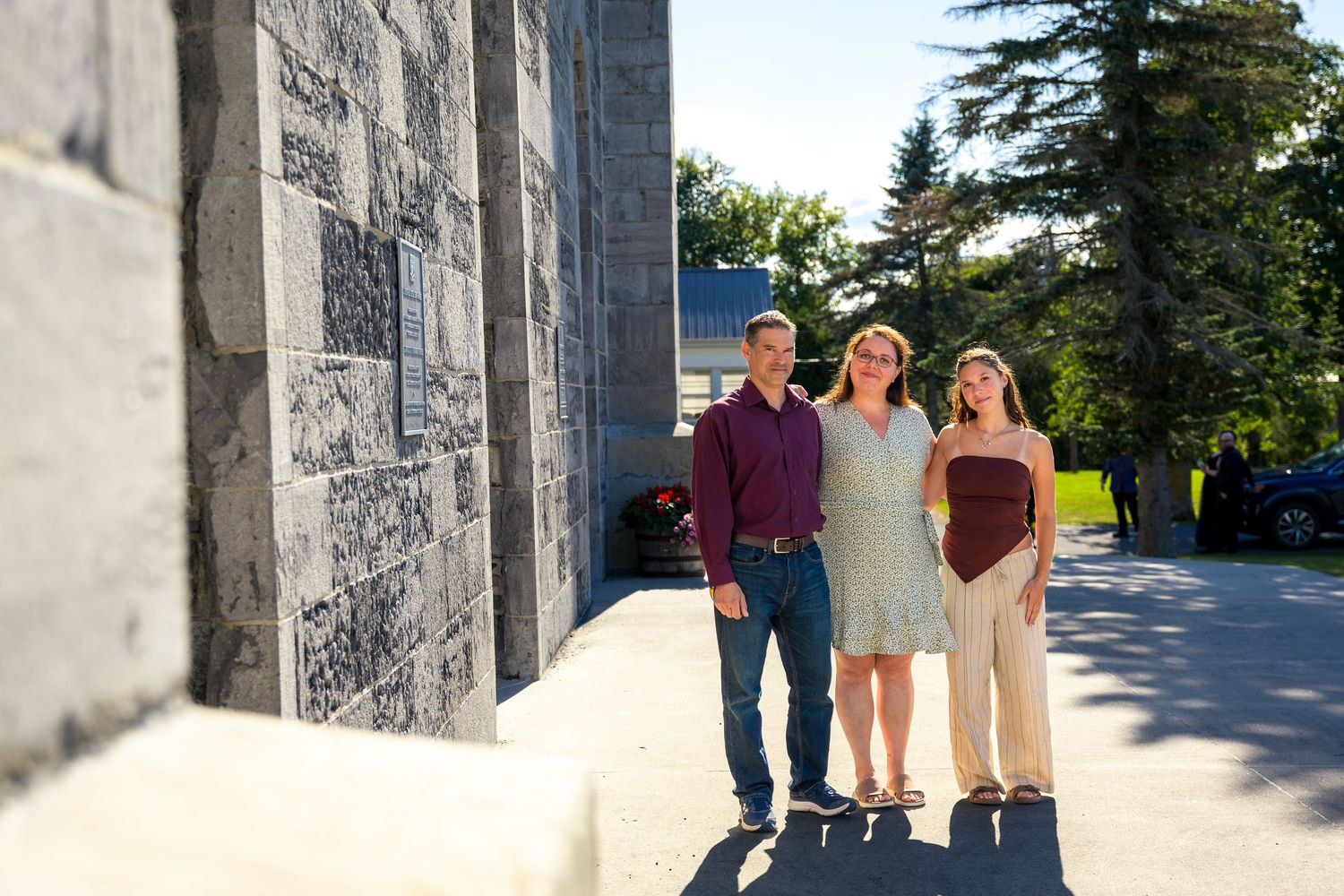 Three people stand together in casual attire against stone building exterior. Ottawa Family Photographer