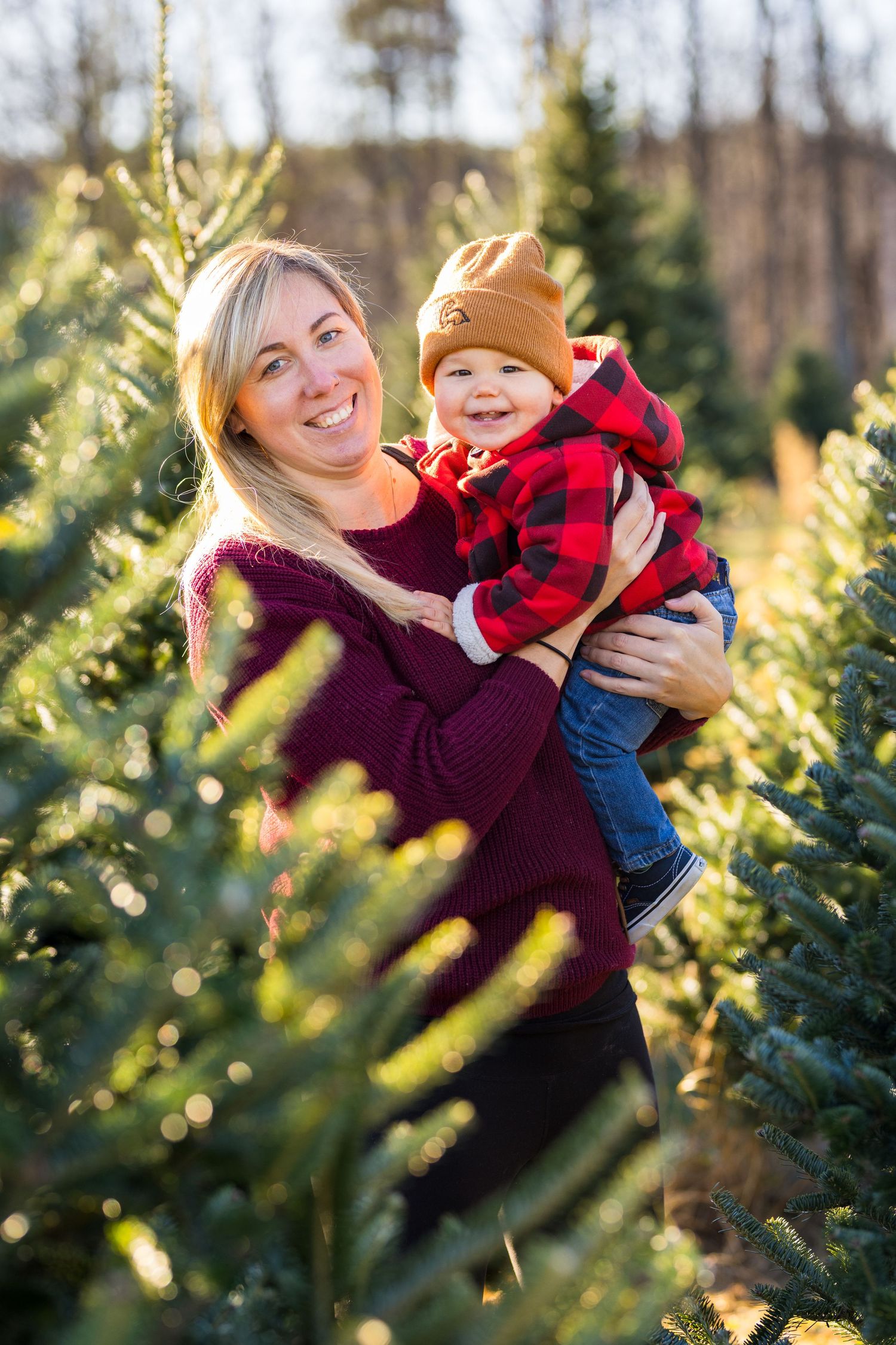 A joyful family moment captured among evergreen trees at a Christmas tree farm on a sunny winter day.