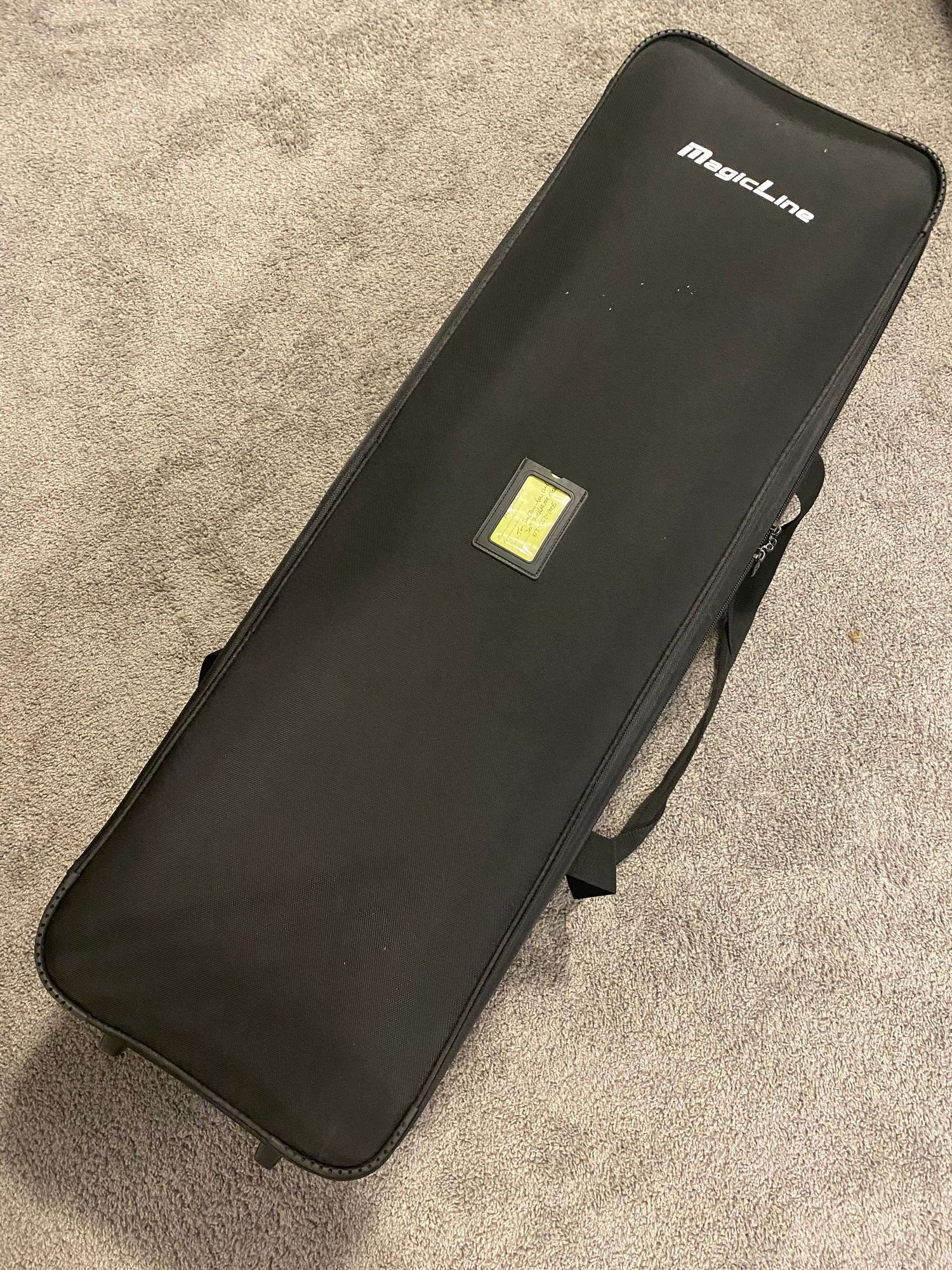 A black  MagicLine Studio XL Bag case with handle and yellow identification badge on a beige carpet.