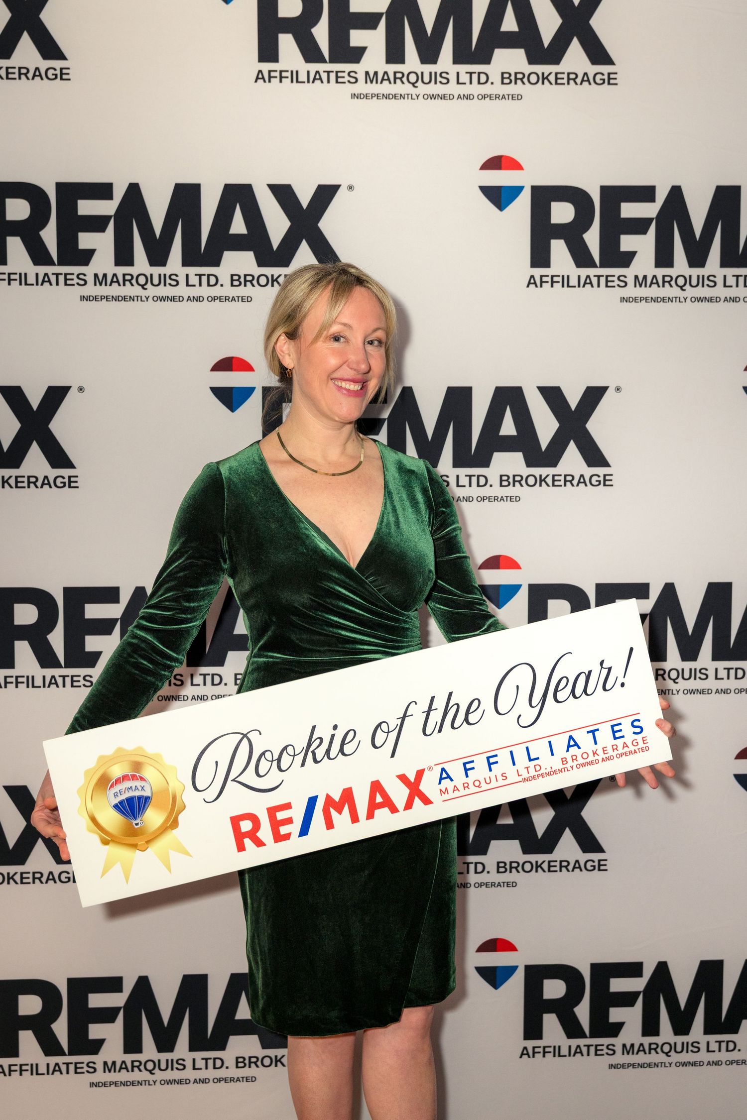 Real estate agent in emerald green dress poses with REMAX branded signage at corporate event. Corporate Event Photography Ottawa