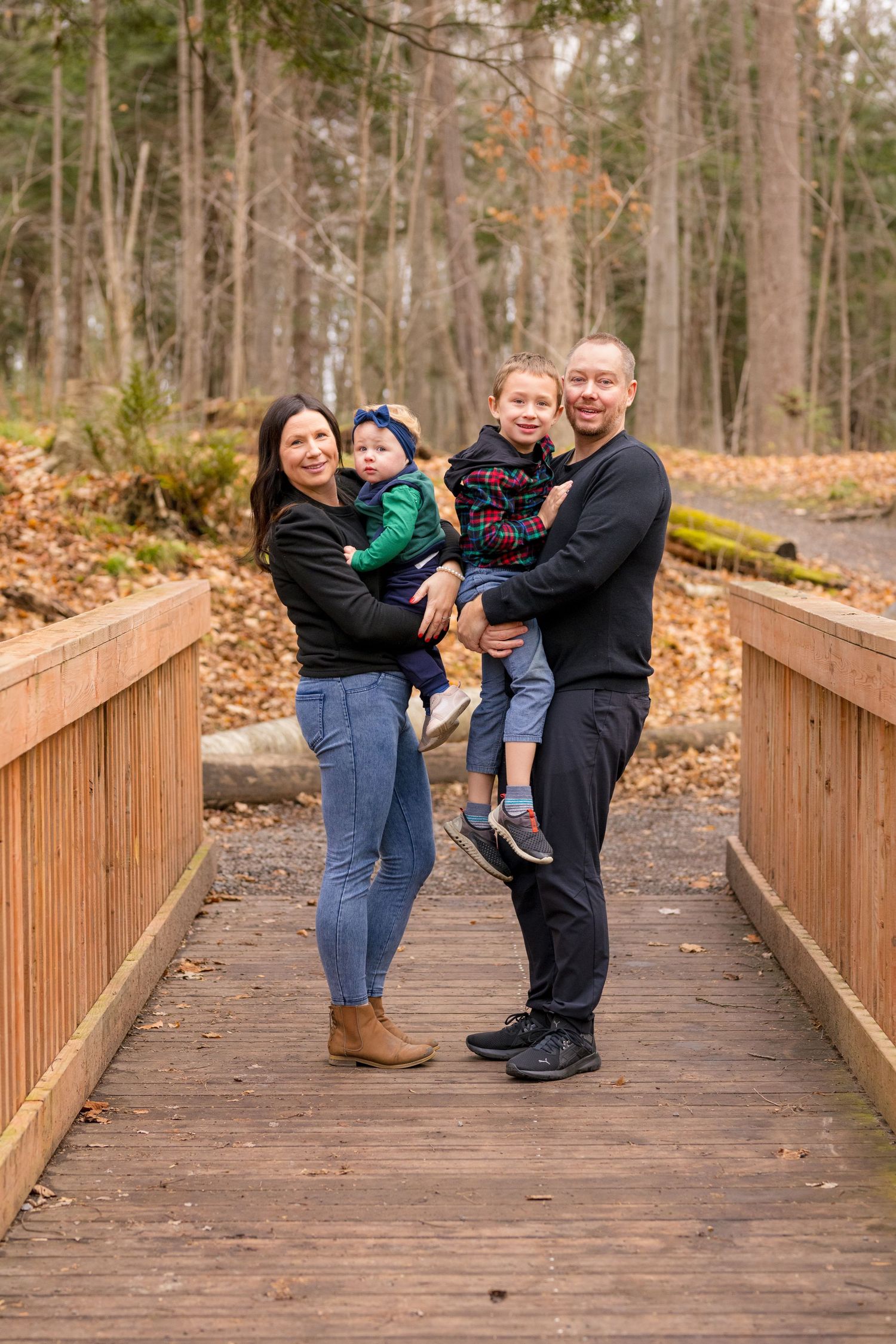 A family poses for photos on a wooden bridge walkway surrounded by autumn trees. Ottawa Family Photographer
