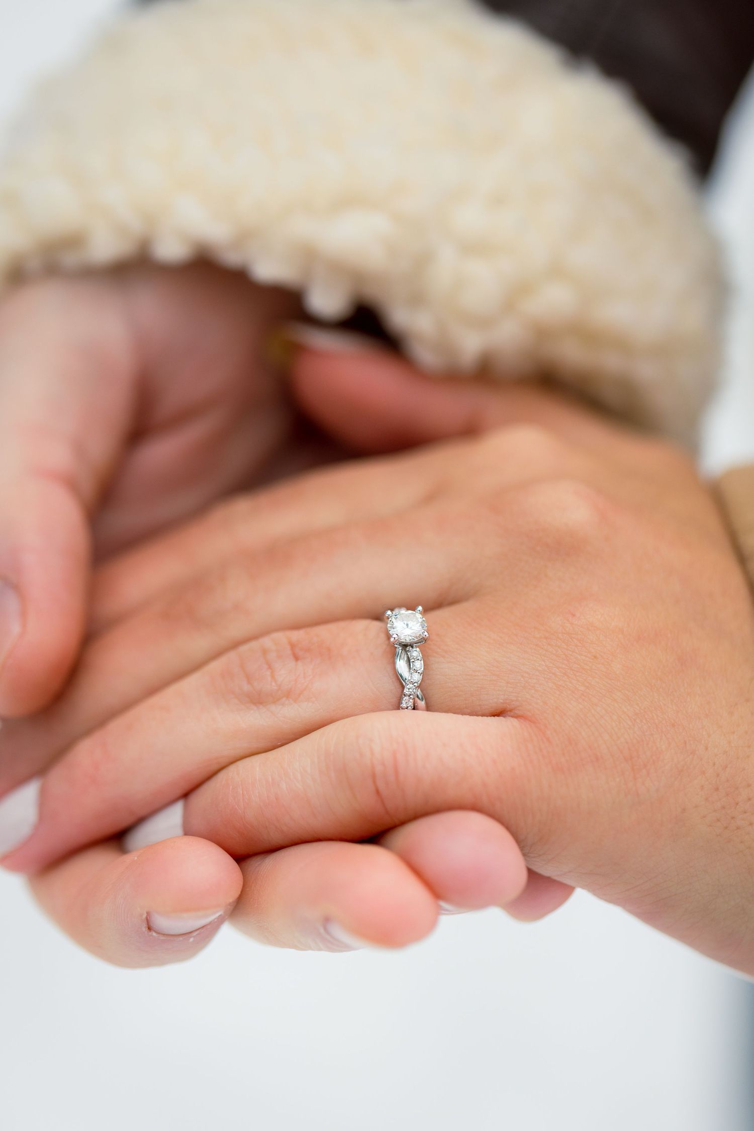 A sparkling engagement ring resting on the bride-to-be’s hand, surrounded by soft snow on a winter day.