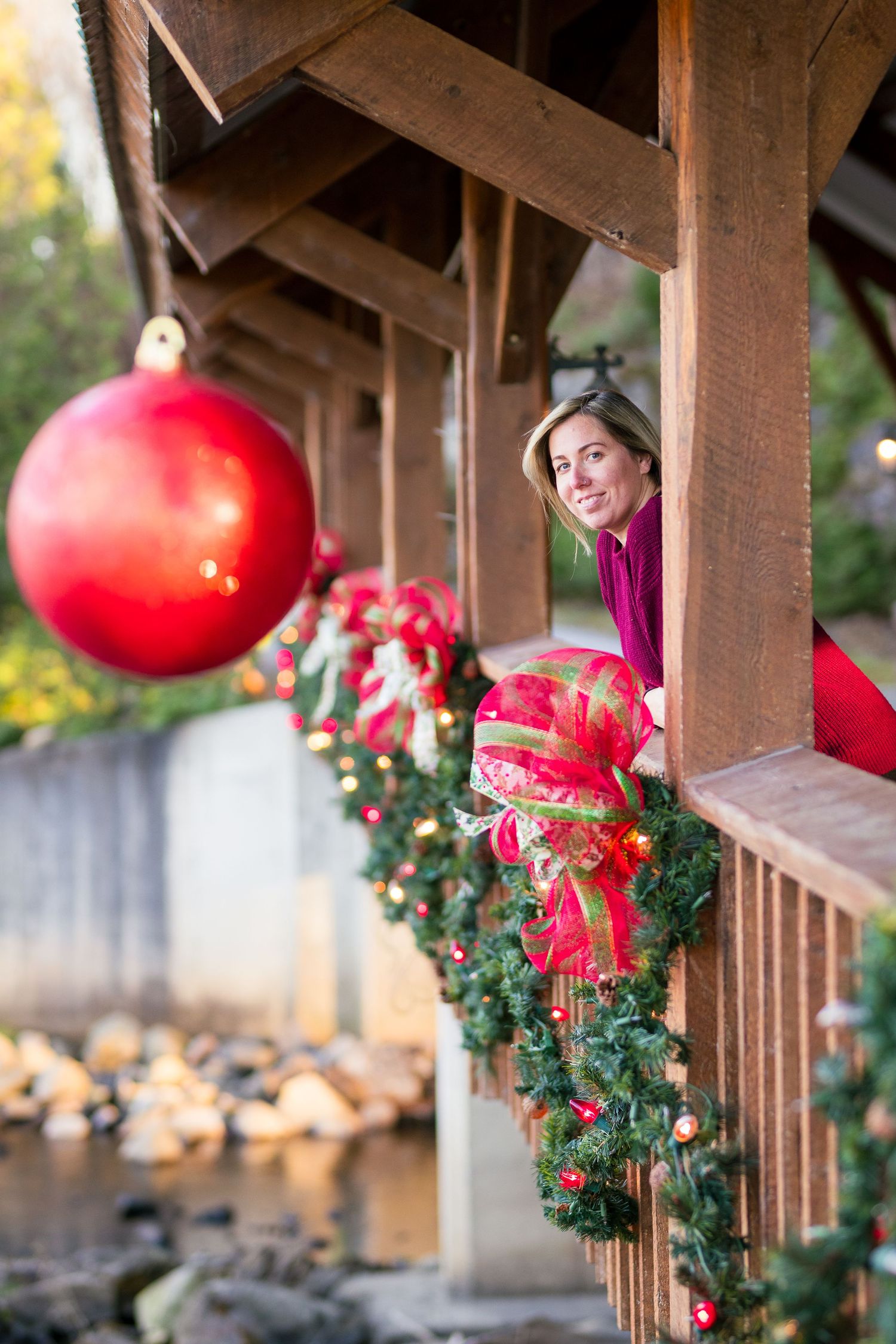 Rustic wooden porch decorated for Christmas with oversized red ornaments, evergreen garland, and festive red bows.