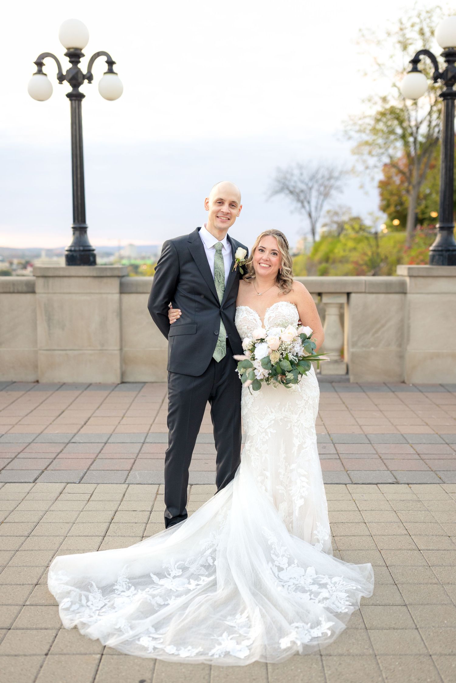 A wedding couple poses together on a stone terrace at the Fairmont Château Laurier with fall trees. Ottawa Wedding Photographer