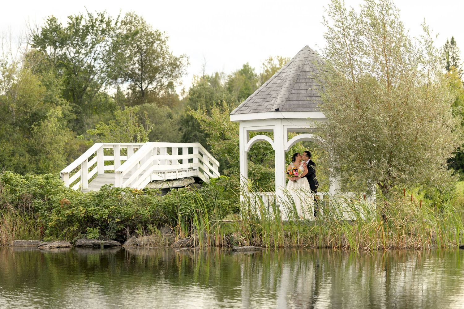 Bride and groom share a romantic moment in a white gazebo at Orchard View Greely. Ottawa Wedding Photographer Tim Gowling