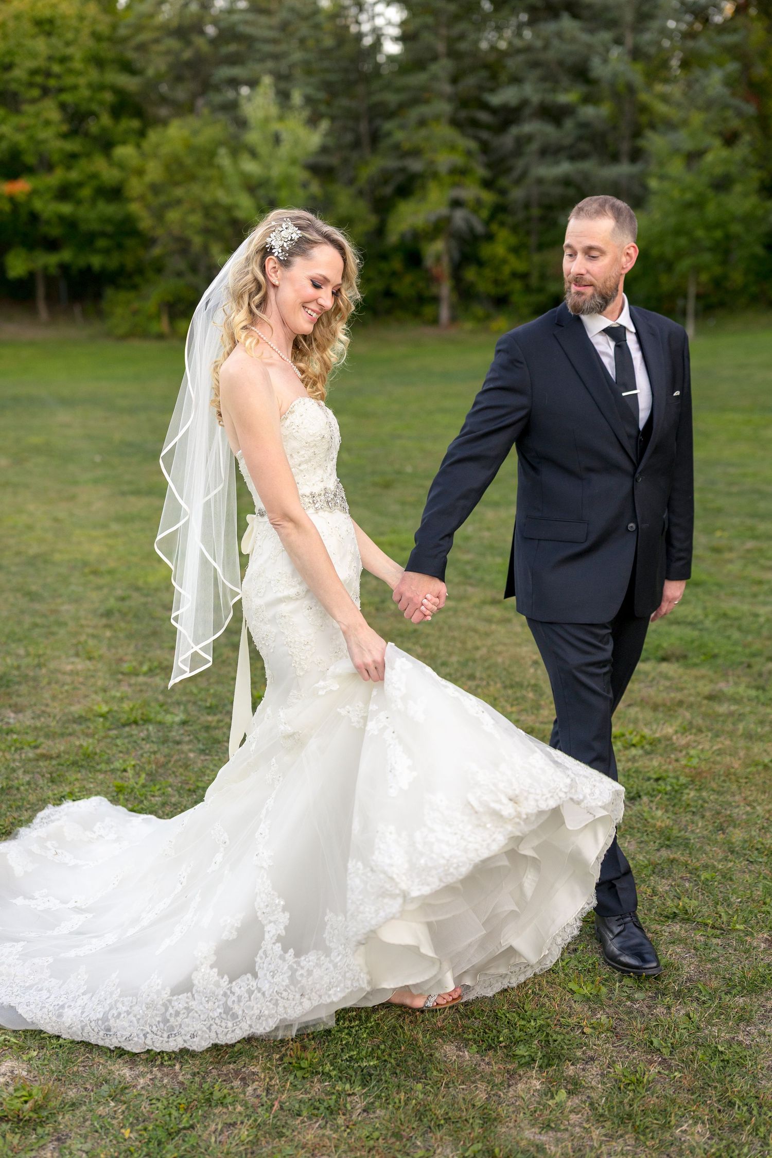 A wedding couple candidly poses in a grassy field with trees in the background. Ottawa Wedding Photographer Tim Gowling