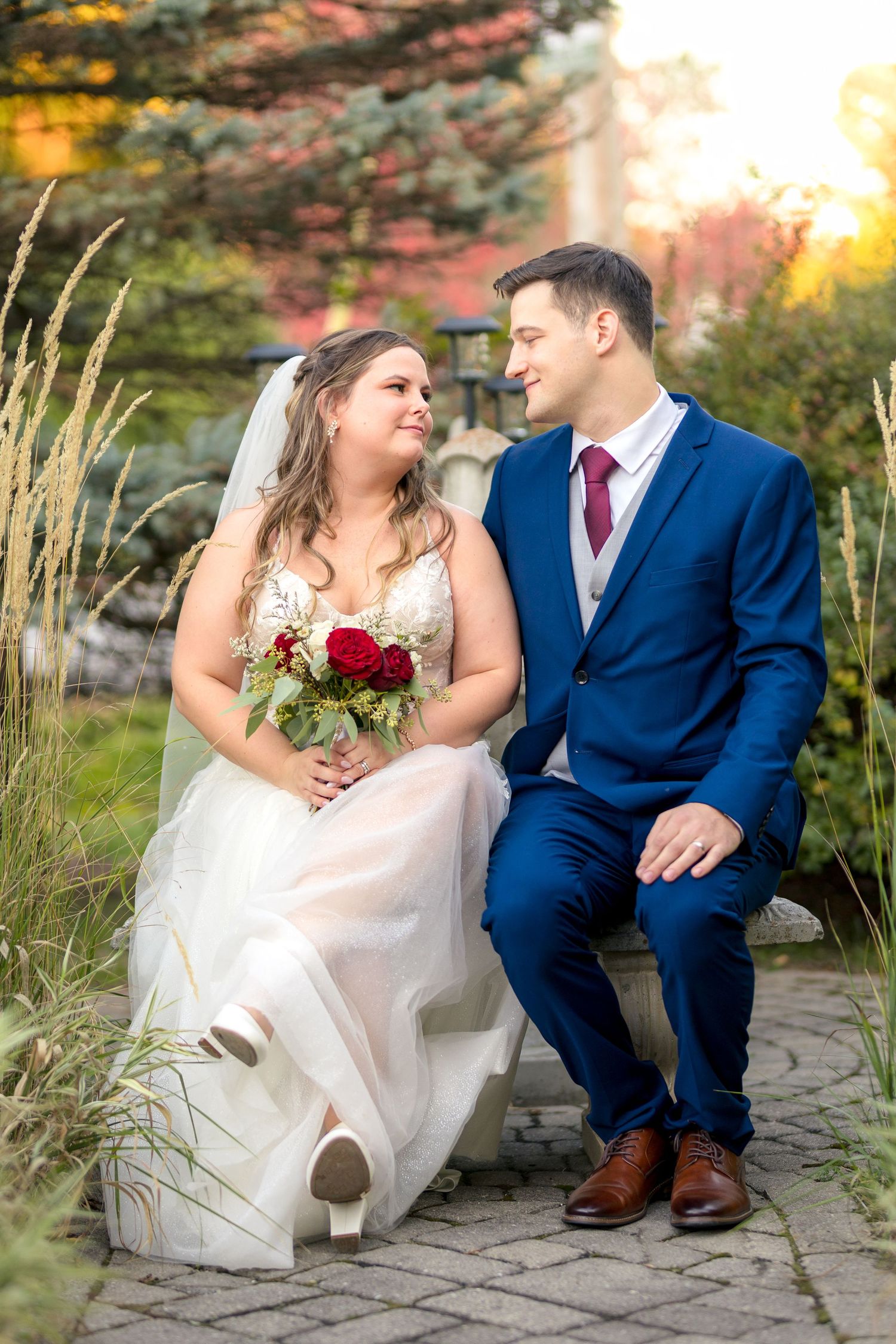 Romantic wedding couple sits together on a stone bench at sunset surrounded by autumn foliage. Ottawa Wedding Photographer