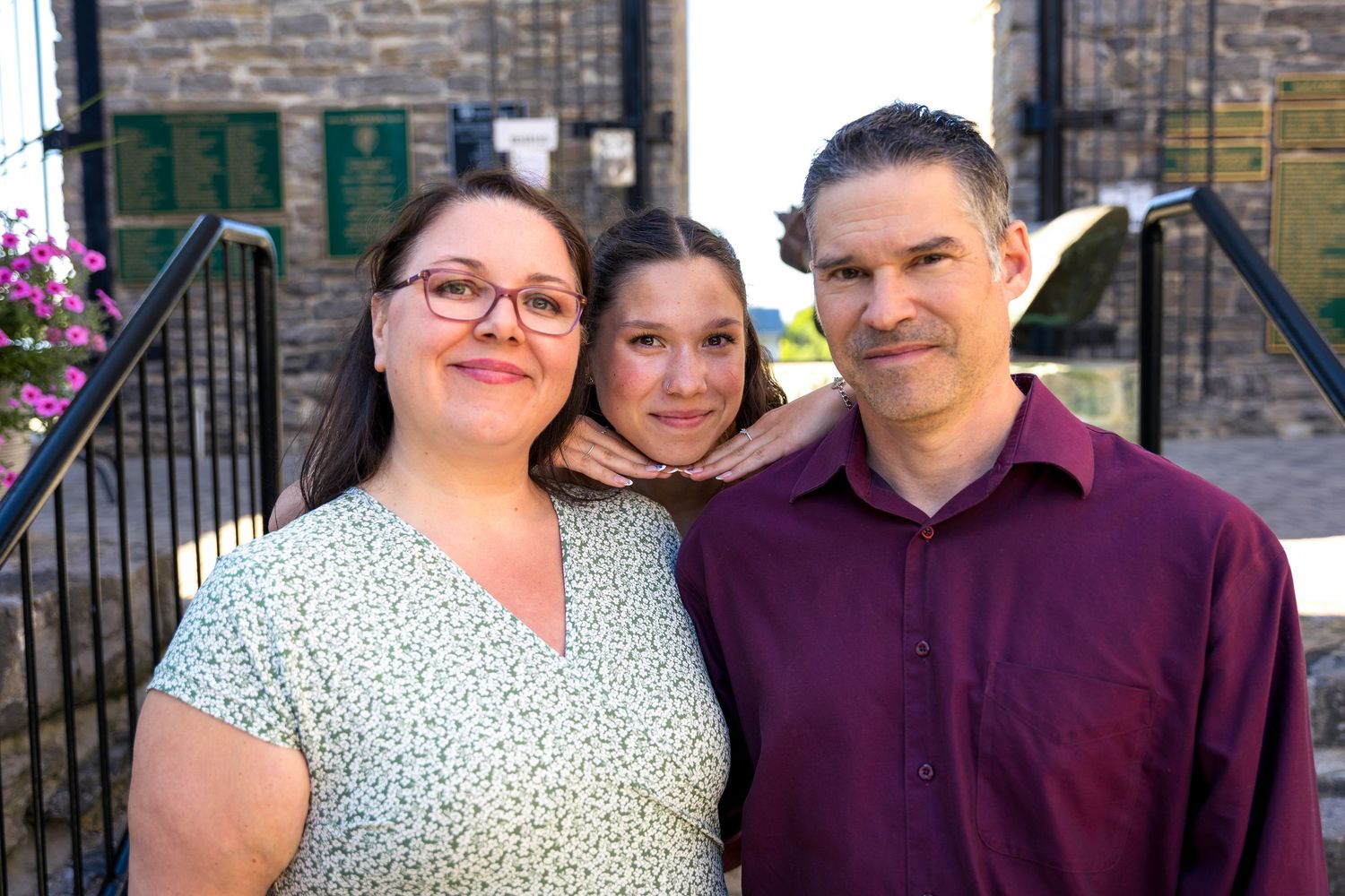 Three people smile together outdoors against brick building backdrop. Ottawa Family Photographer