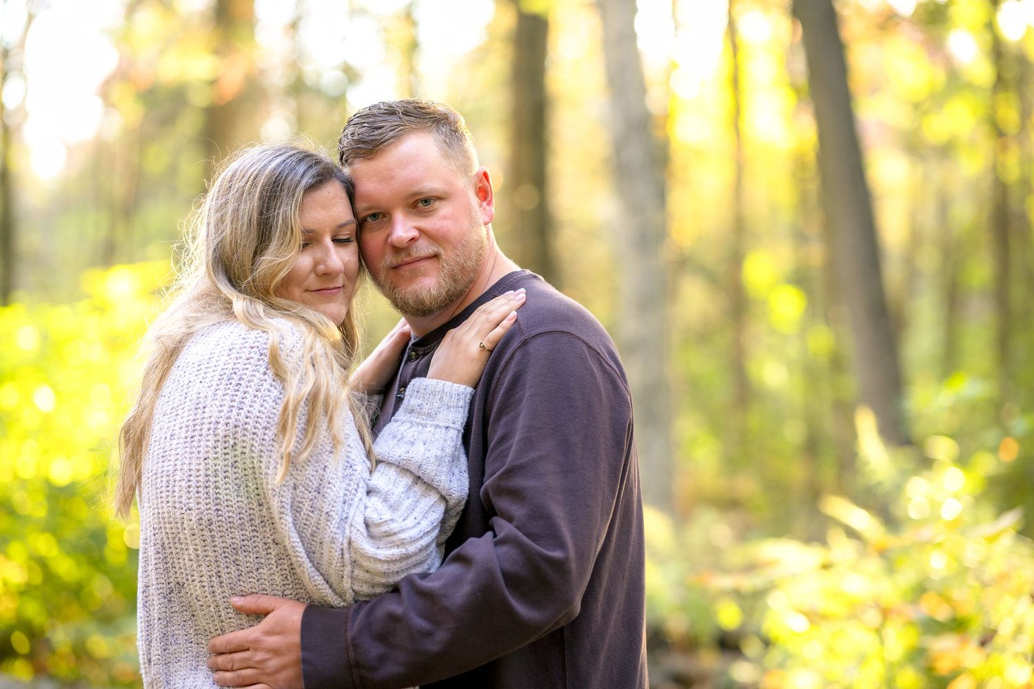 Couple embracing in sunlit autumn forest setting. Ottawa Portrait Photographer