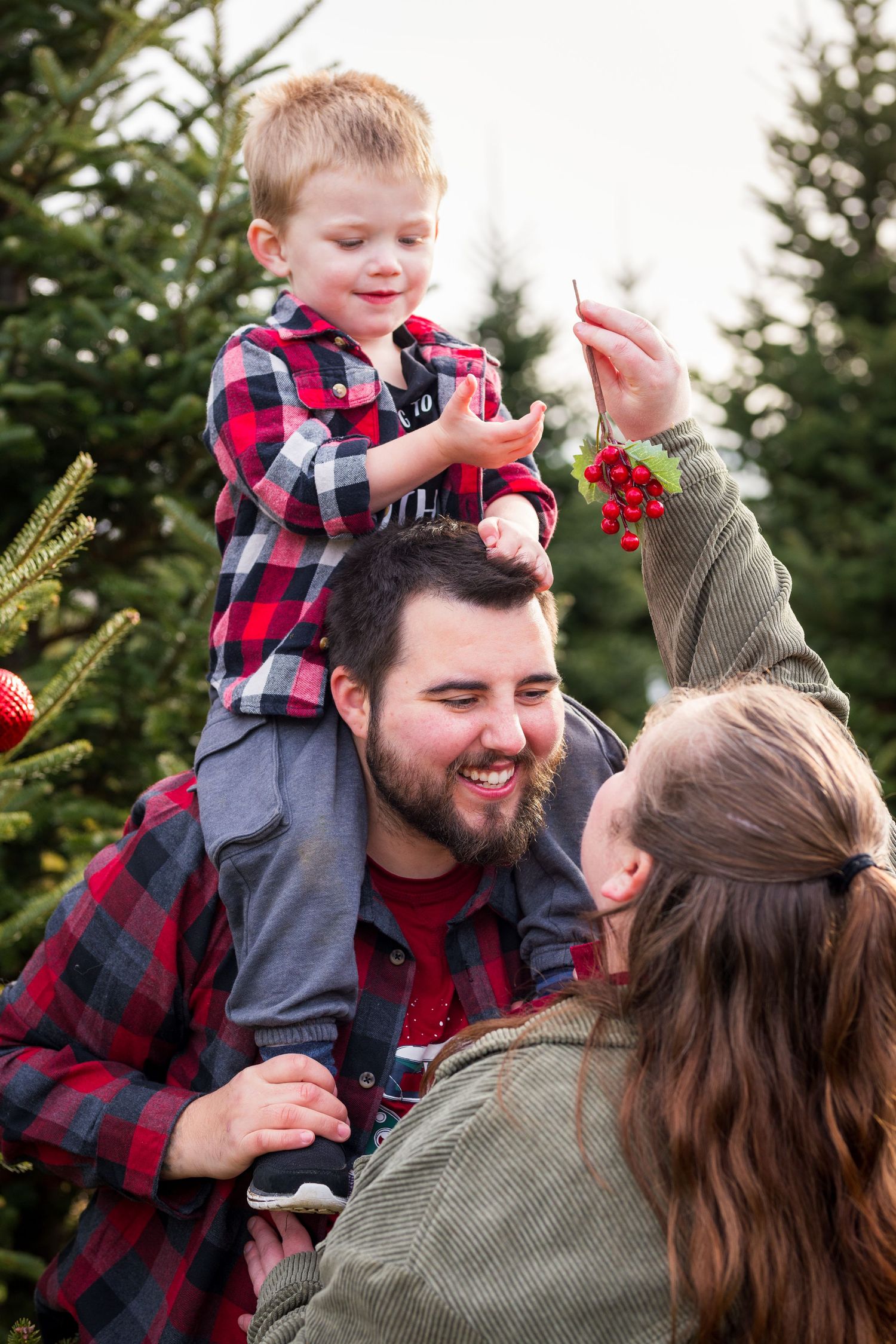 Family shares joyful moment together during Christmas photoshoot at evergreen tree farm with festive decorations.