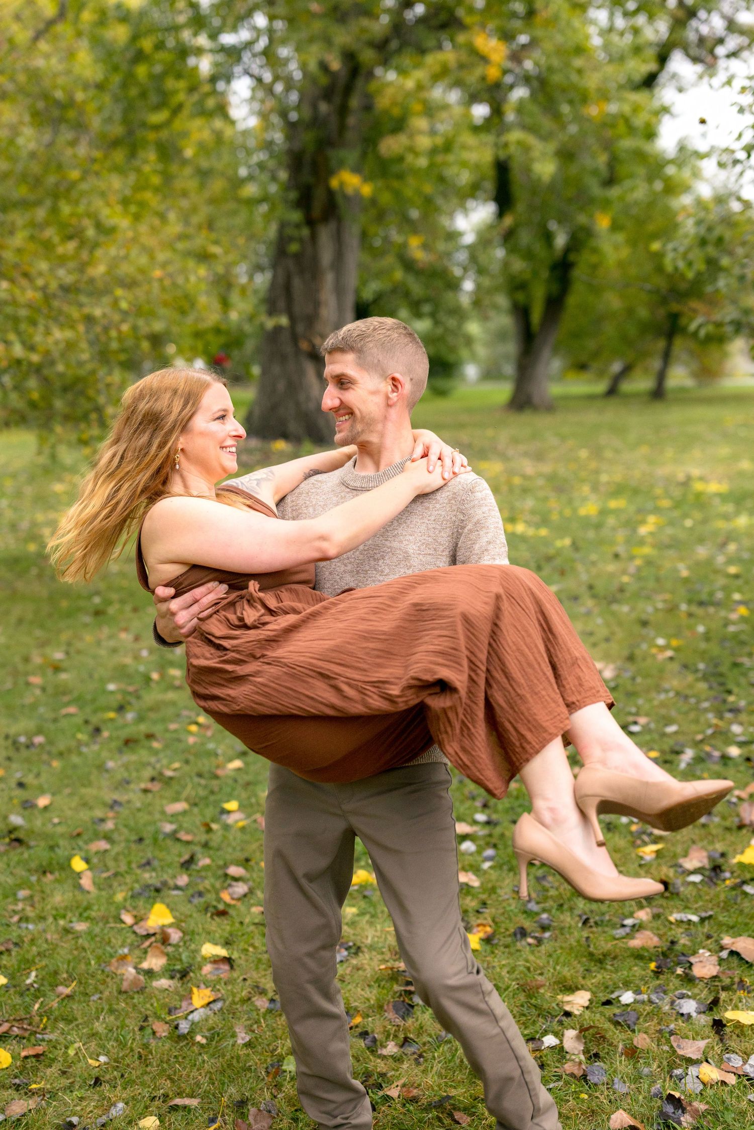 Playful couple dancing and spinning in a park with autumn leaves and trees in the background. Ottawa Wedding Photographer
