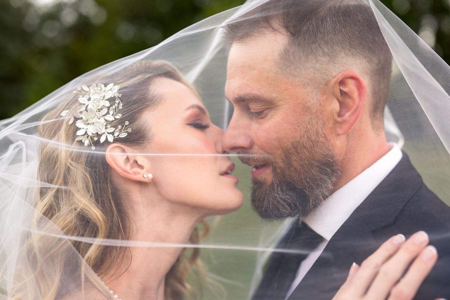 A romantic wedding moment captured under a flowing veil with the bride wearing a sparkly hair accessory. Ottawa Wedding Photographer