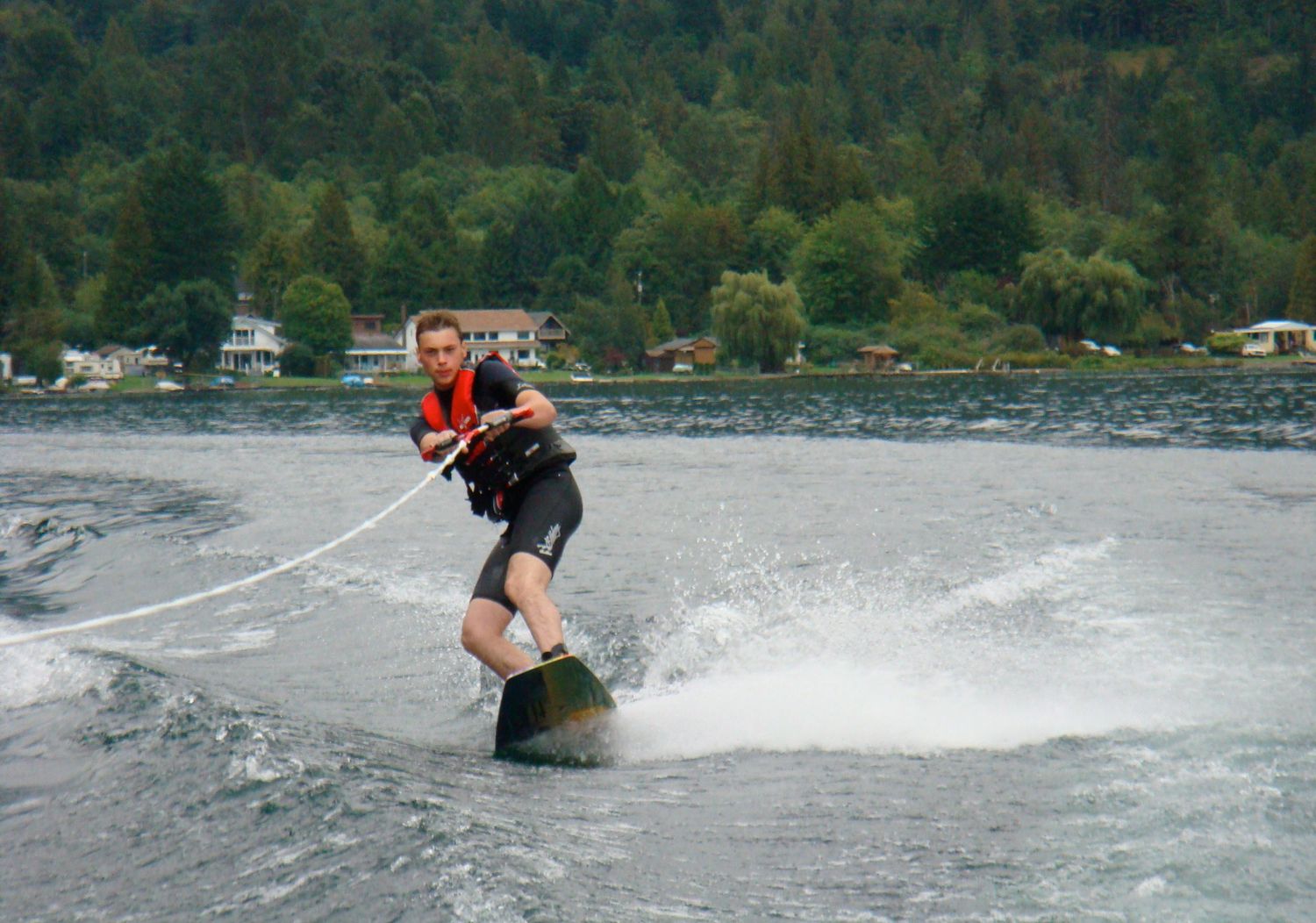 Ottawa wedding & portrait photographer wakeboarding across a lake, creating a spray of water while performing tricks on a sunny day.