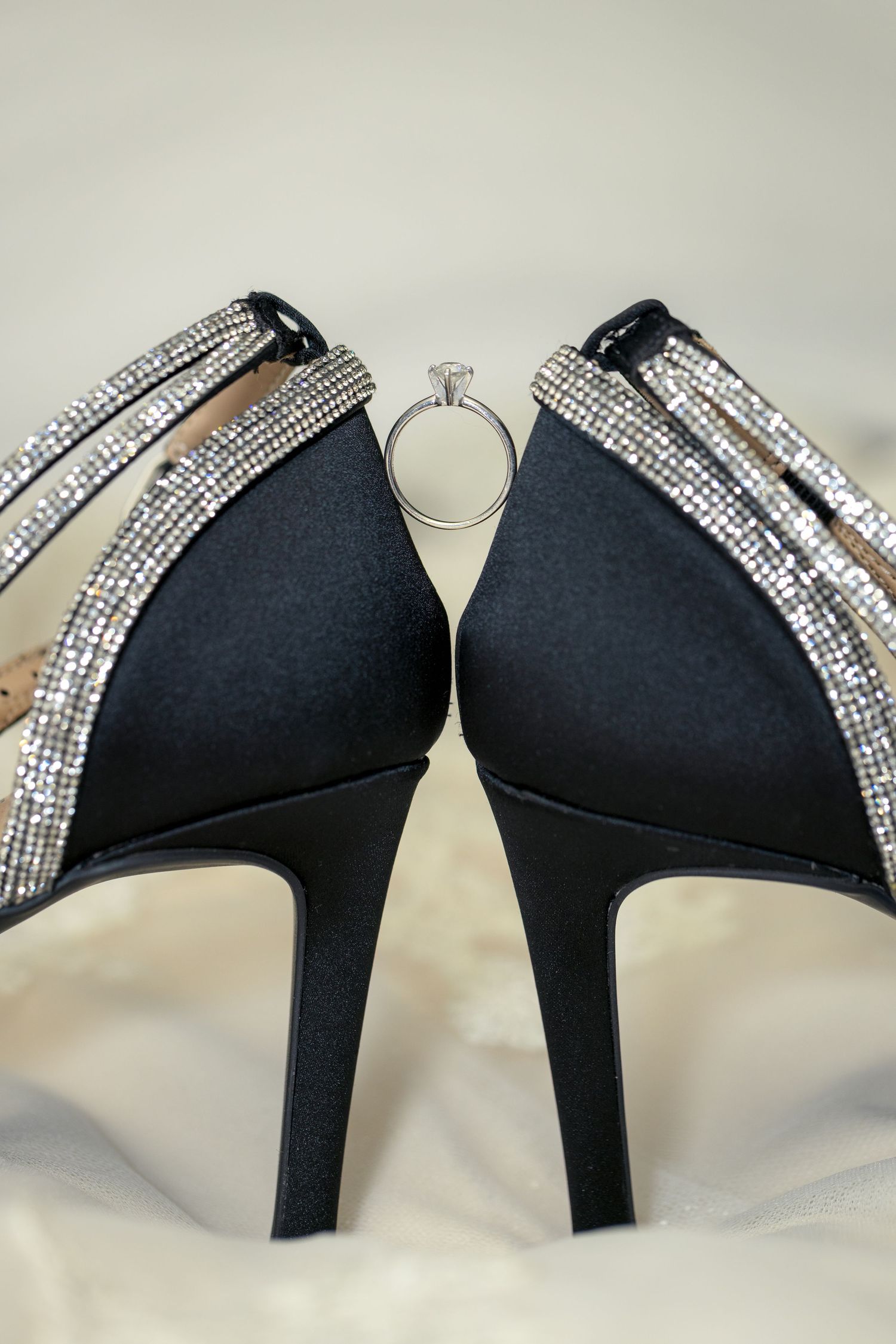 Black high heel shoes decorated with sparkling rhinestone trim holding an engagement ring on a wedding dress Ottawa wedding photographer