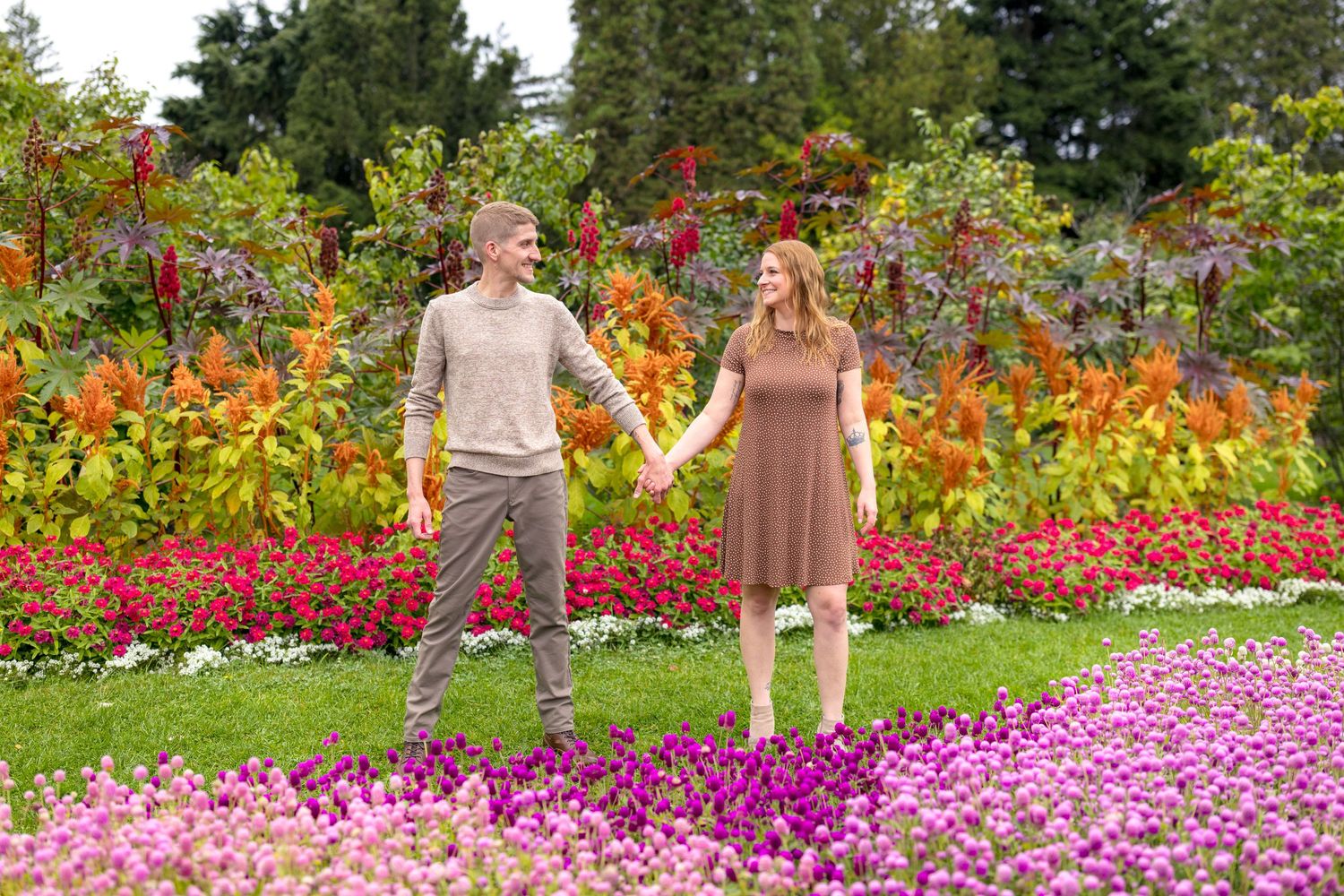 A couple stands together in a garden surrounded by vibrant orange and pink flowers. Ottawa Wedding Photographer